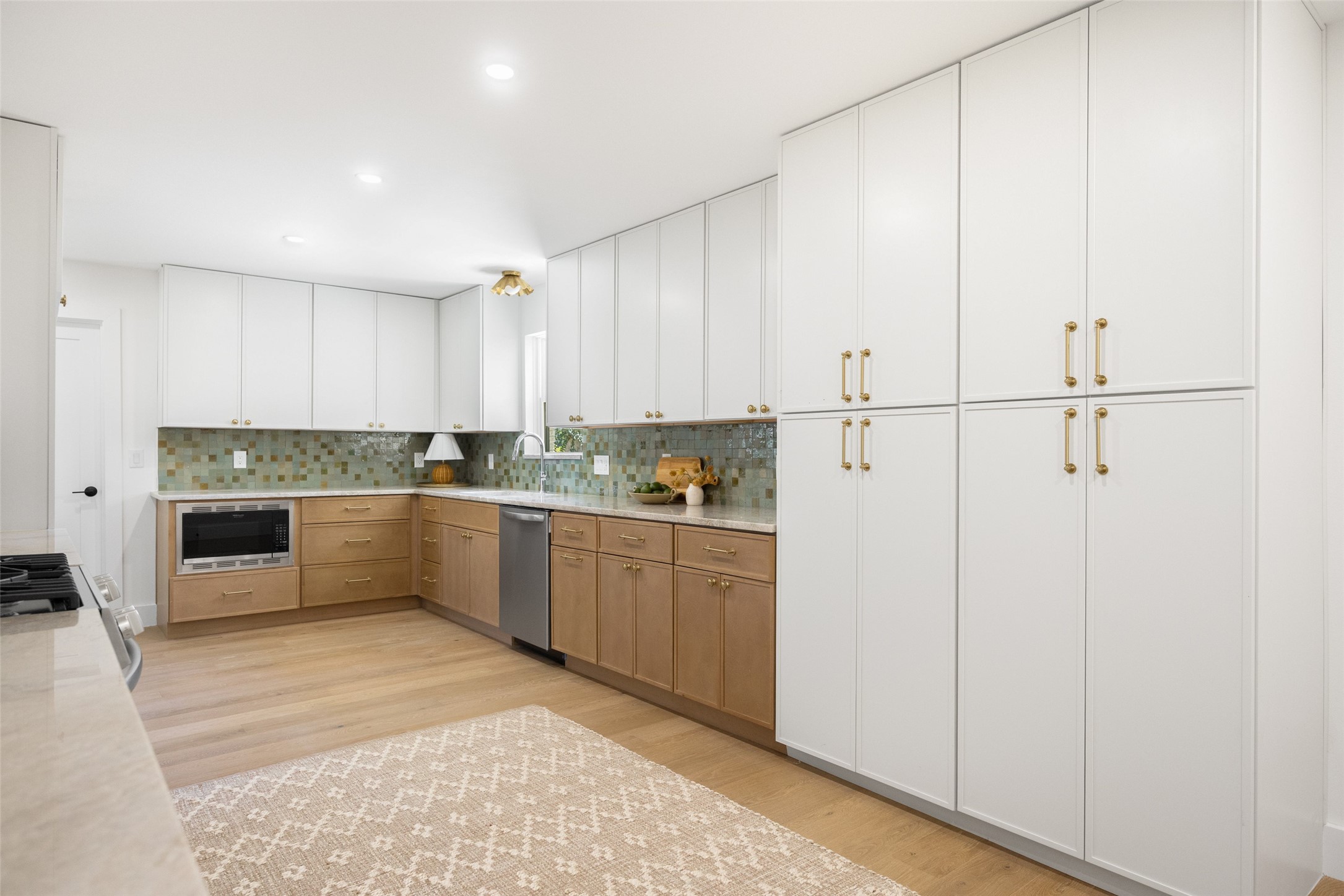 Kitchen with white cabinetry, wood lower cabinets, green mosaic backsplash, and light wood flooring.