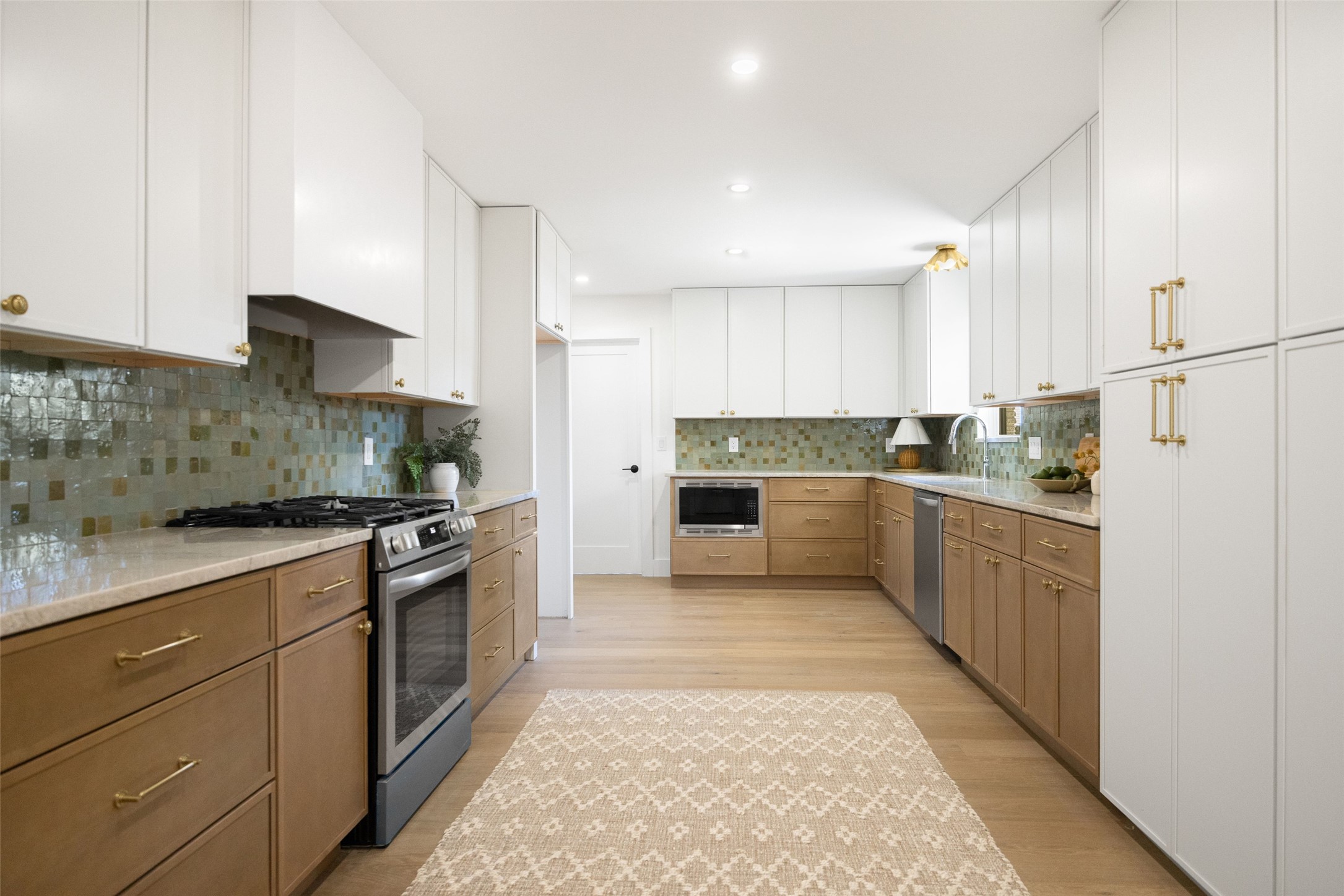 Bright kitchen with white upper cabinets, warm wood lower cabinets, and a green-gray mosaic backsplash.