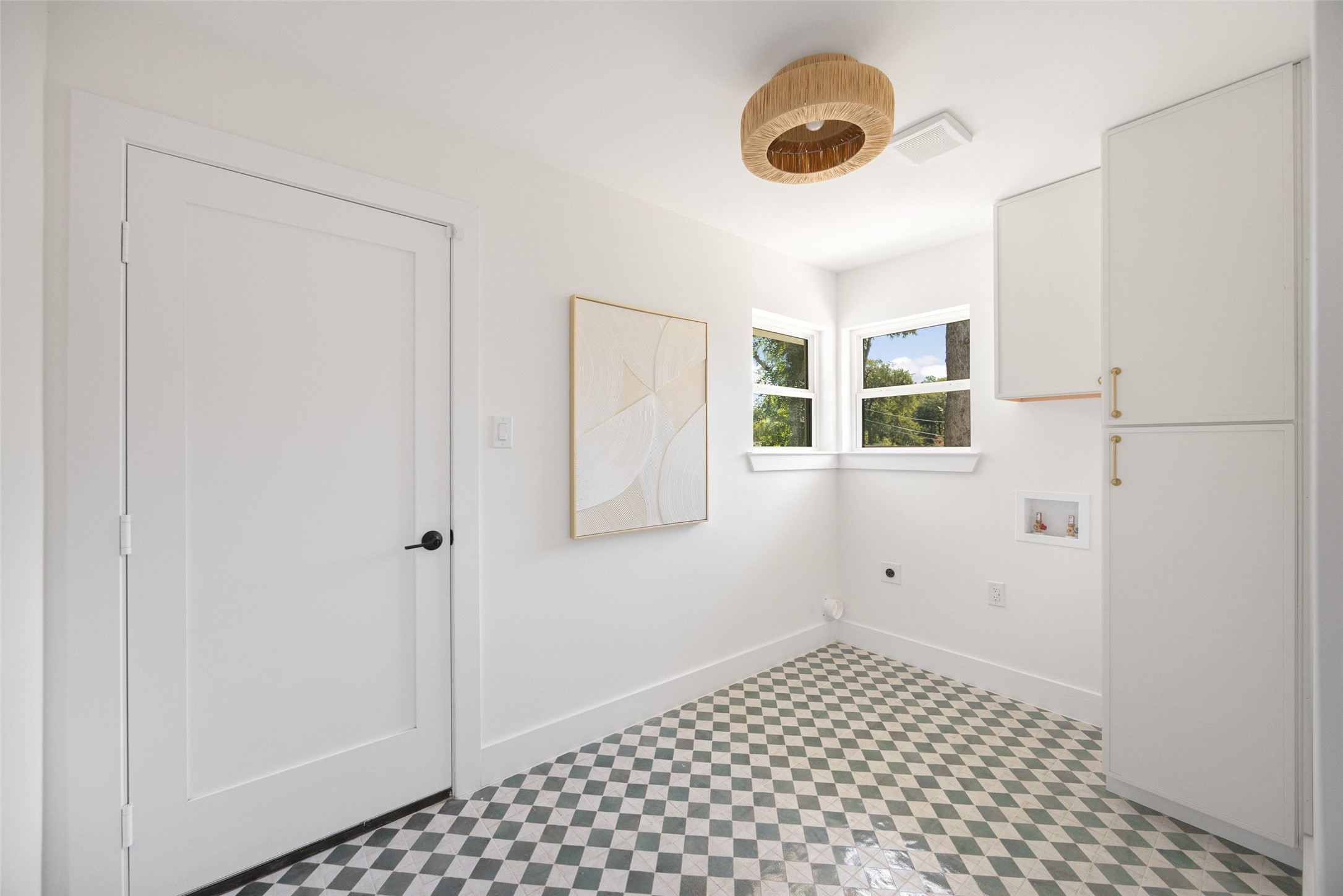 Laundry room with white cabinets, corner windows, and checkerboard tile flooring.