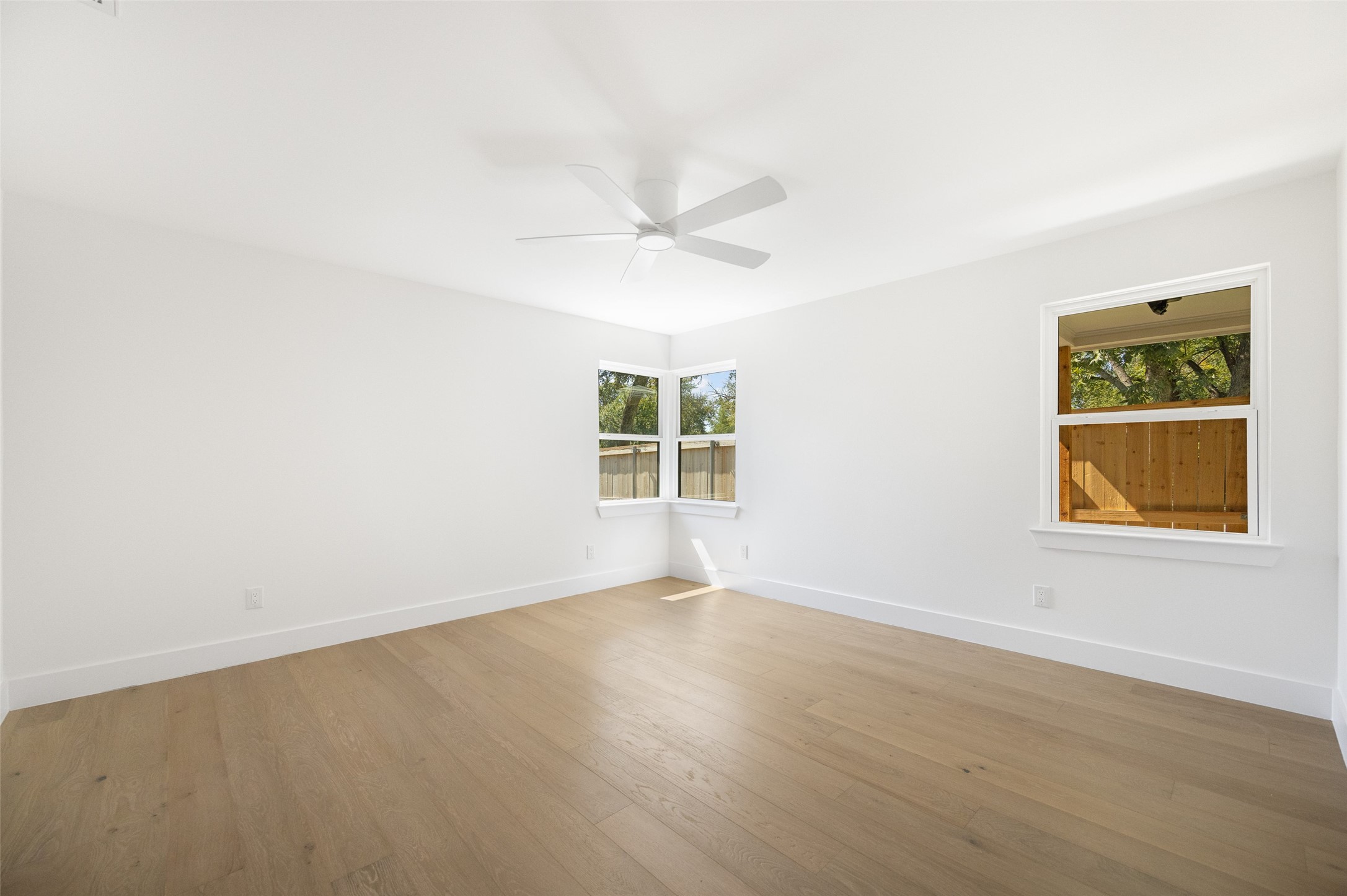 Empty room with light wood floors, a ceiling fan, and corner windows.