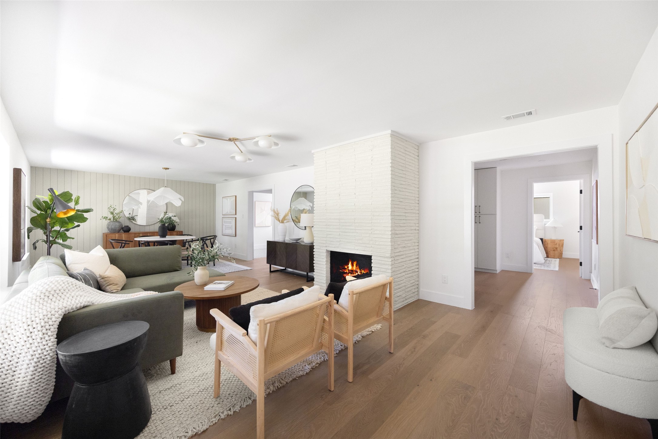 Open-plan living room with a white brick fireplace, green sofa, cane chairs, and dining area.