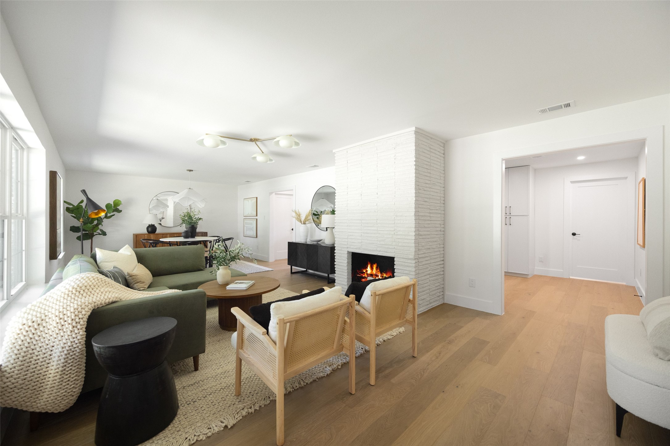 Living room with a green sectional, cane chairs, and a lit fireplace in a white brick partition.