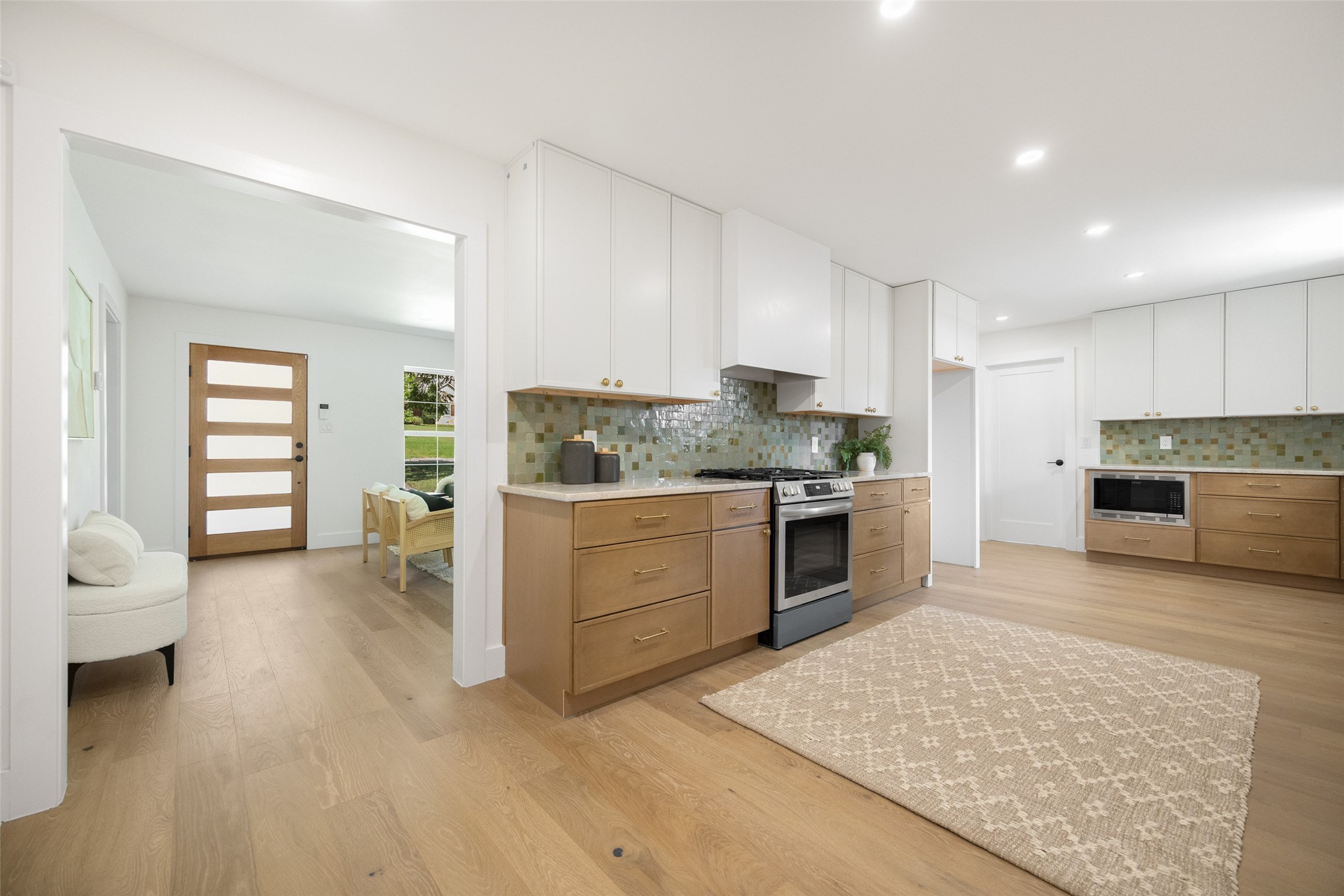 Bright kitchen with wood cabinets, green tile backsplash, stainless steel range, and a large rug.