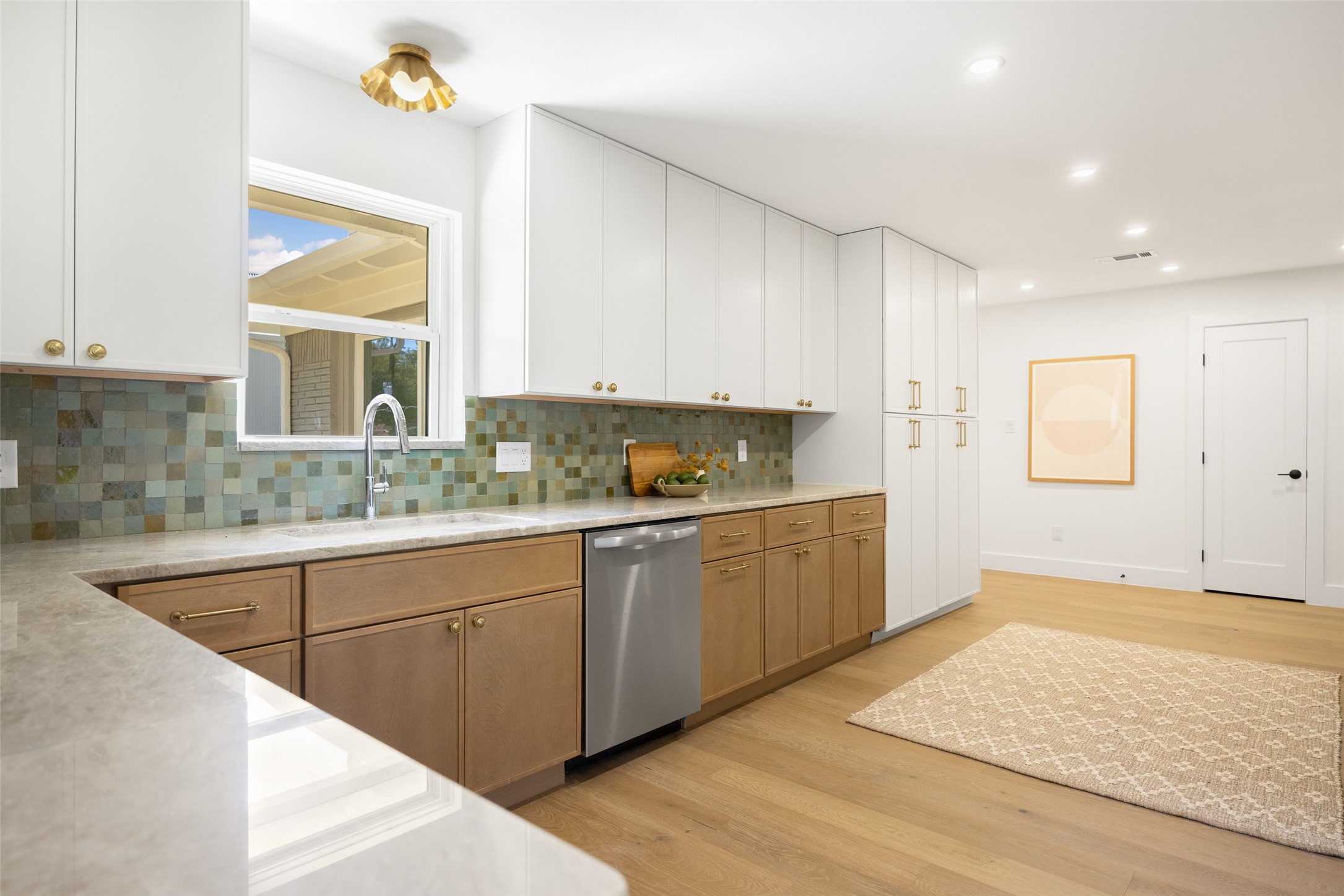 Kitchen with wood and white cabinets, colorful tile backsplash, and a window above the sink.