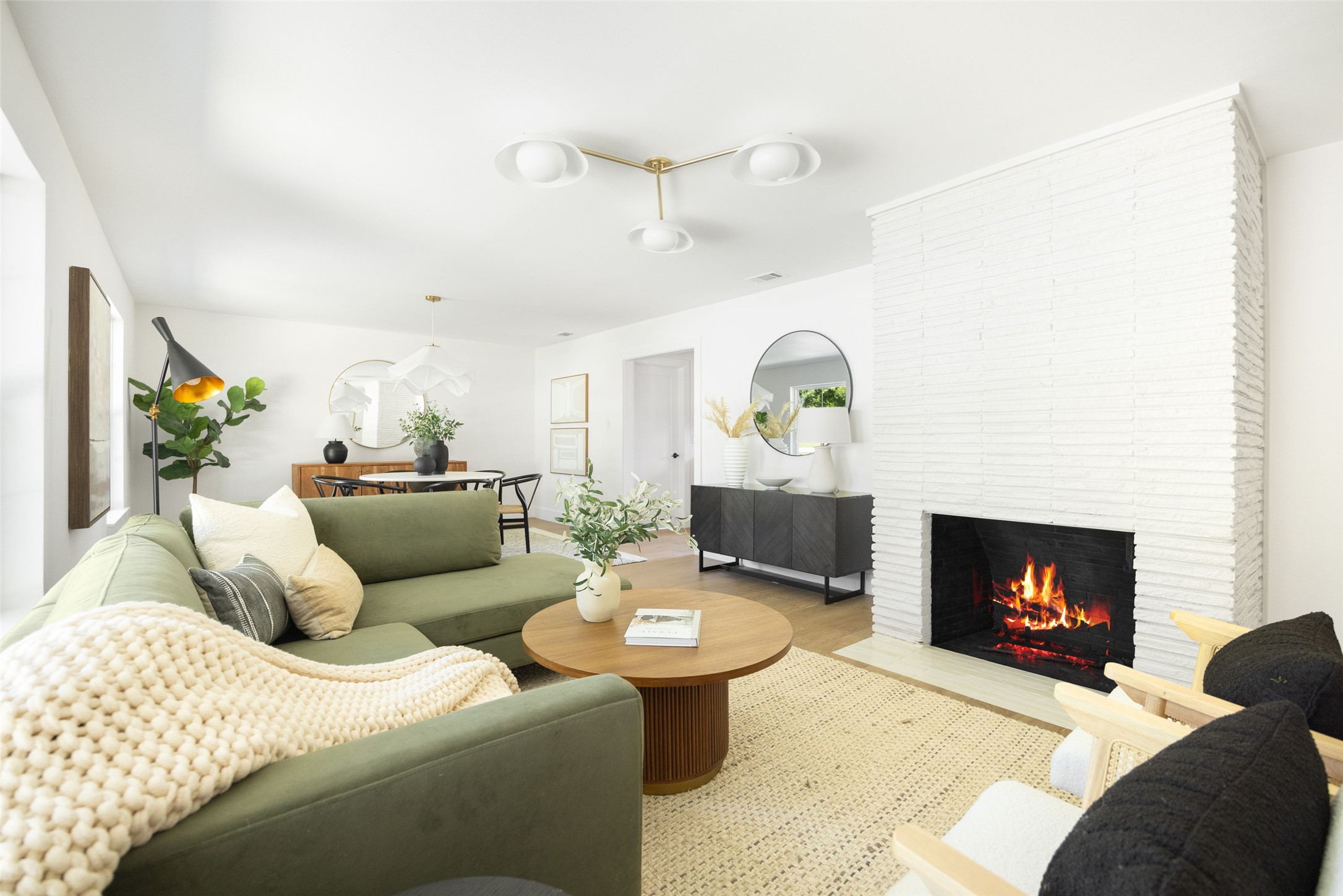 Staged living room with green sectional and lit fireplace in a white brick wall.