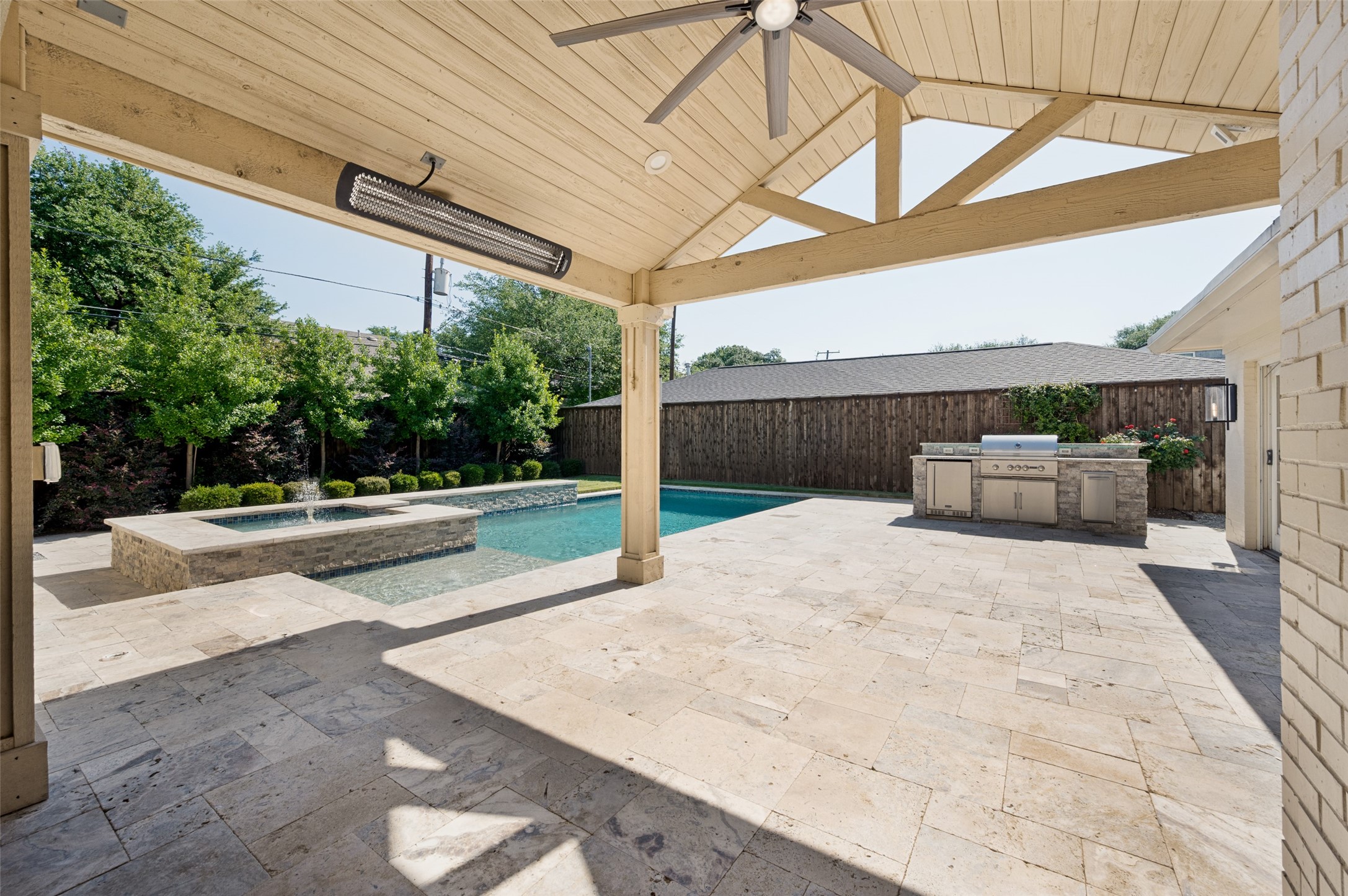 Covered stone patio overlooking a pool and raised spa, with an outdoor kitchen and built-in grill.