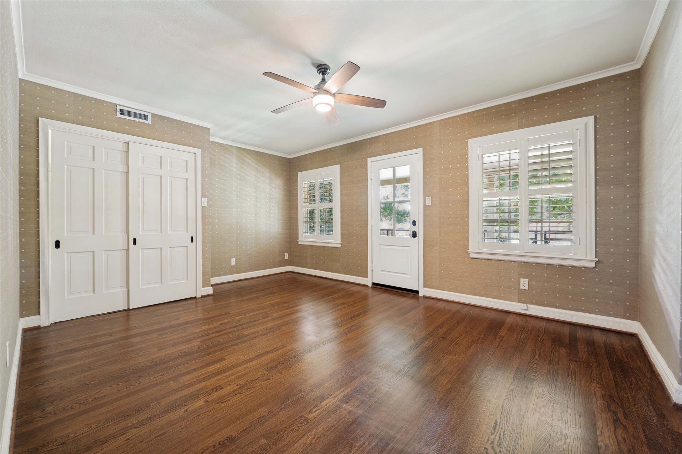 Empty room with dark hardwood floors, white closet doors, plantation shutters, and a ceiling fan.