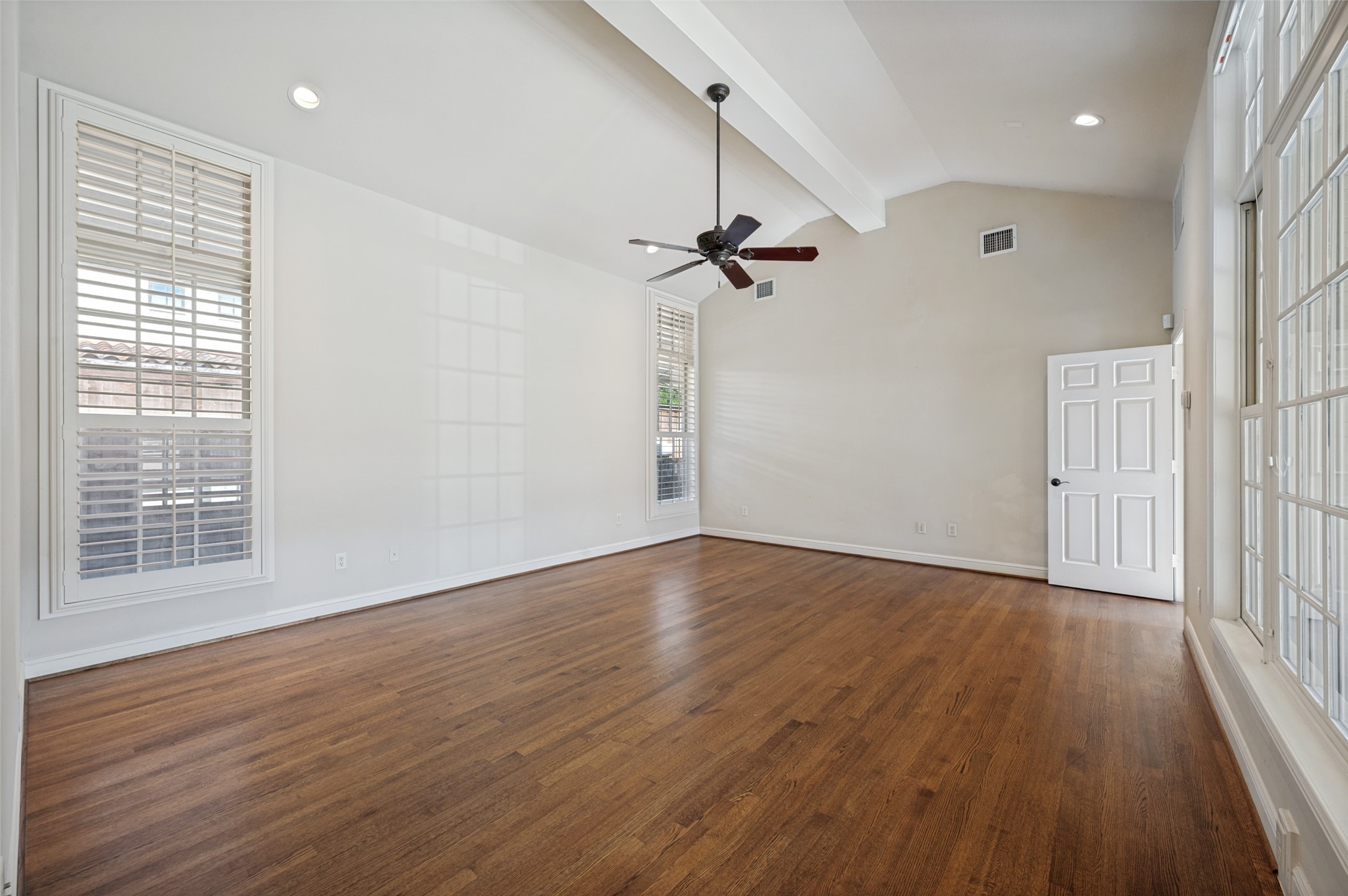 Empty room with hardwood floors, vaulted ceiling, ceiling fan, and tall windows.