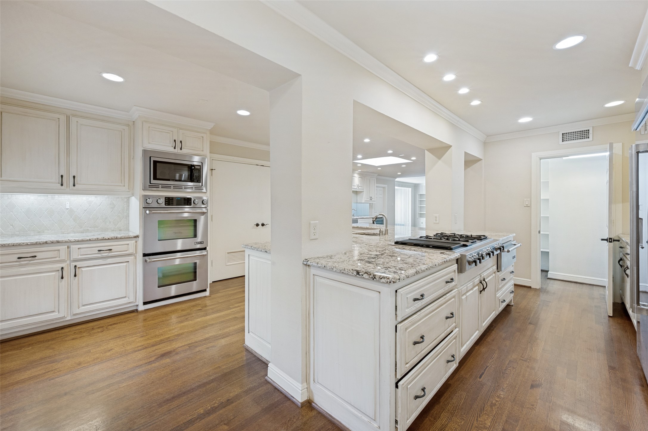 Kitchen with a large granite island and gas cooktop, white cabinetry, stainless double ovens, and hardwood floors.