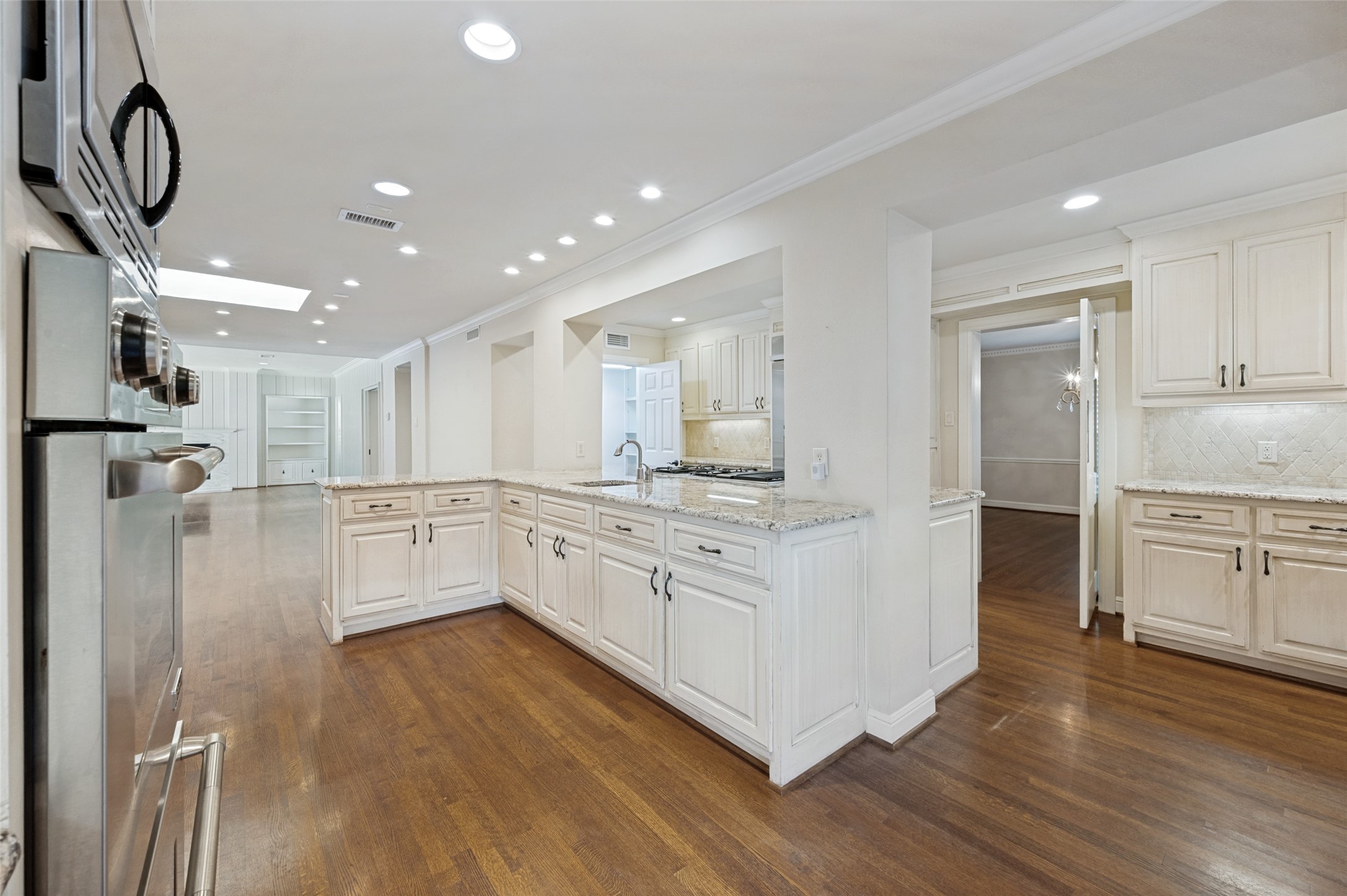 Bright kitchen with a large granite island, white cabinetry, stainless steel appliances, and dark hardwood floors.