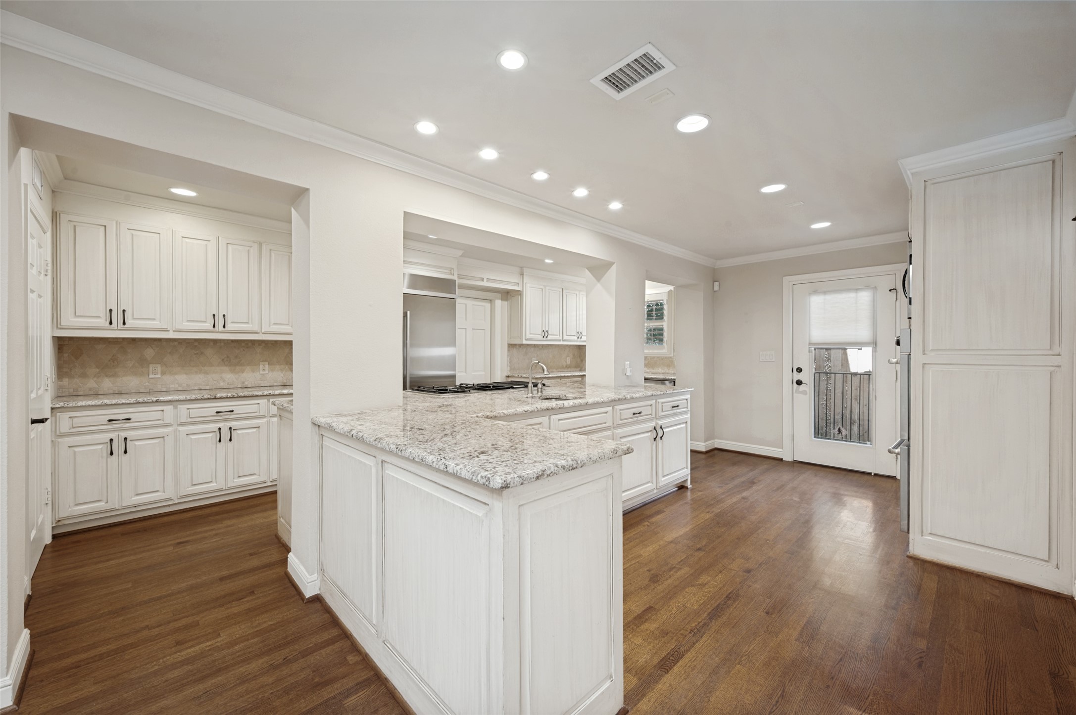 Kitchen with white cabinets, granite counters, a large peninsula, stainless appliances, and dark wood floors.