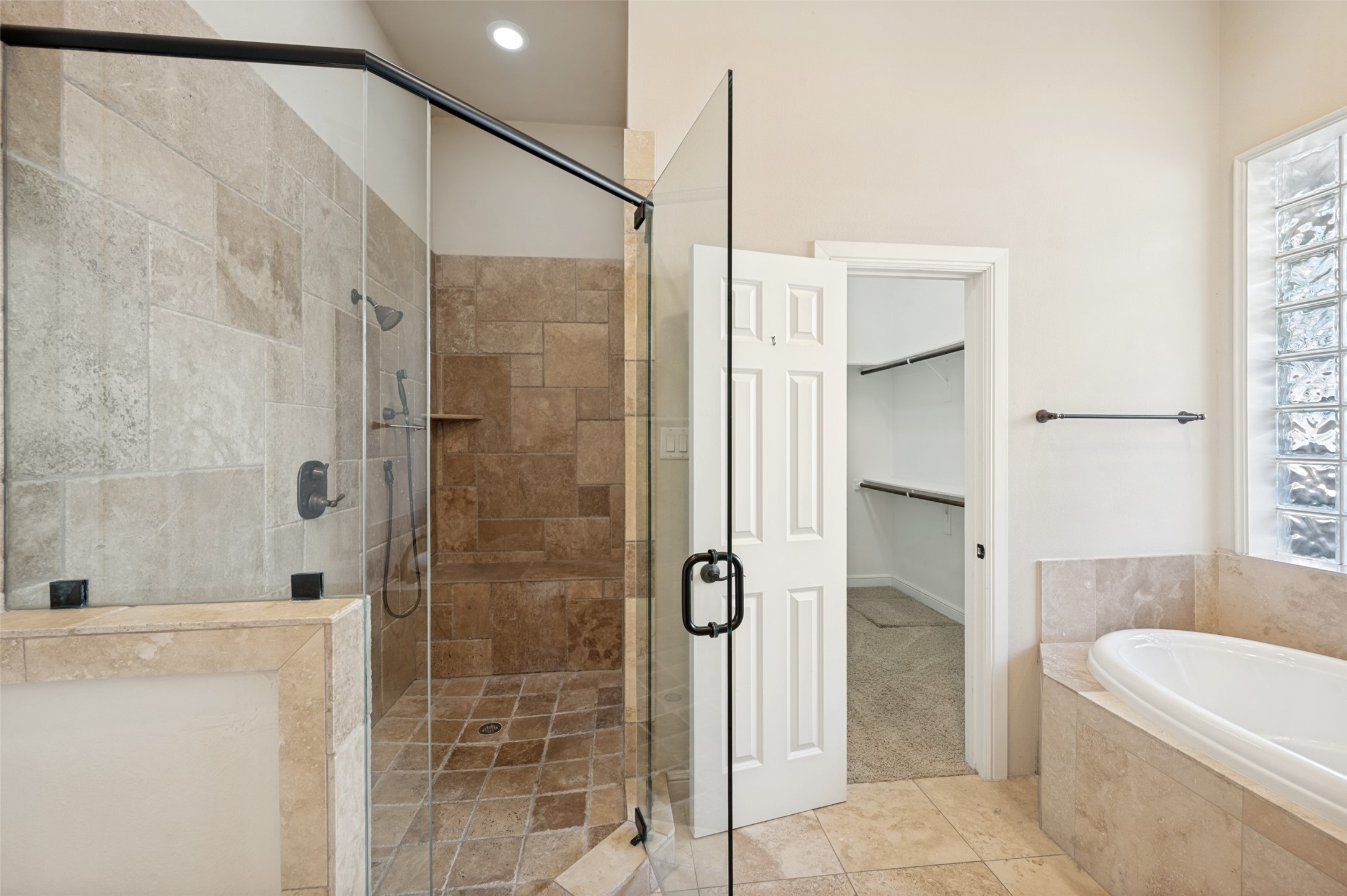 Bathroom with a glass-enclosed stone-tiled shower, built-in tub, and glass-block window.