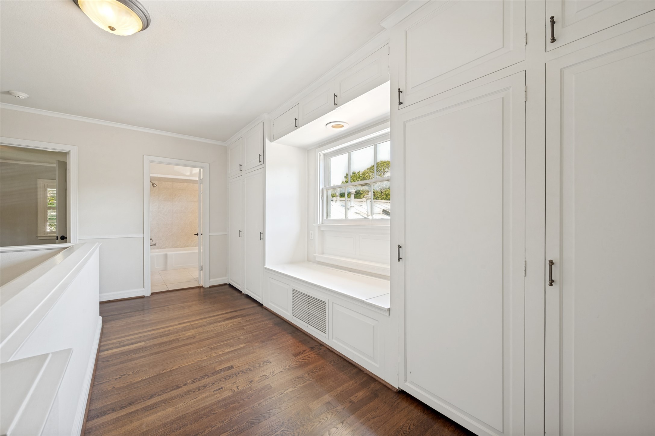 Bright room with white built-in cabinets, a window seat, and dark hardwood floors.