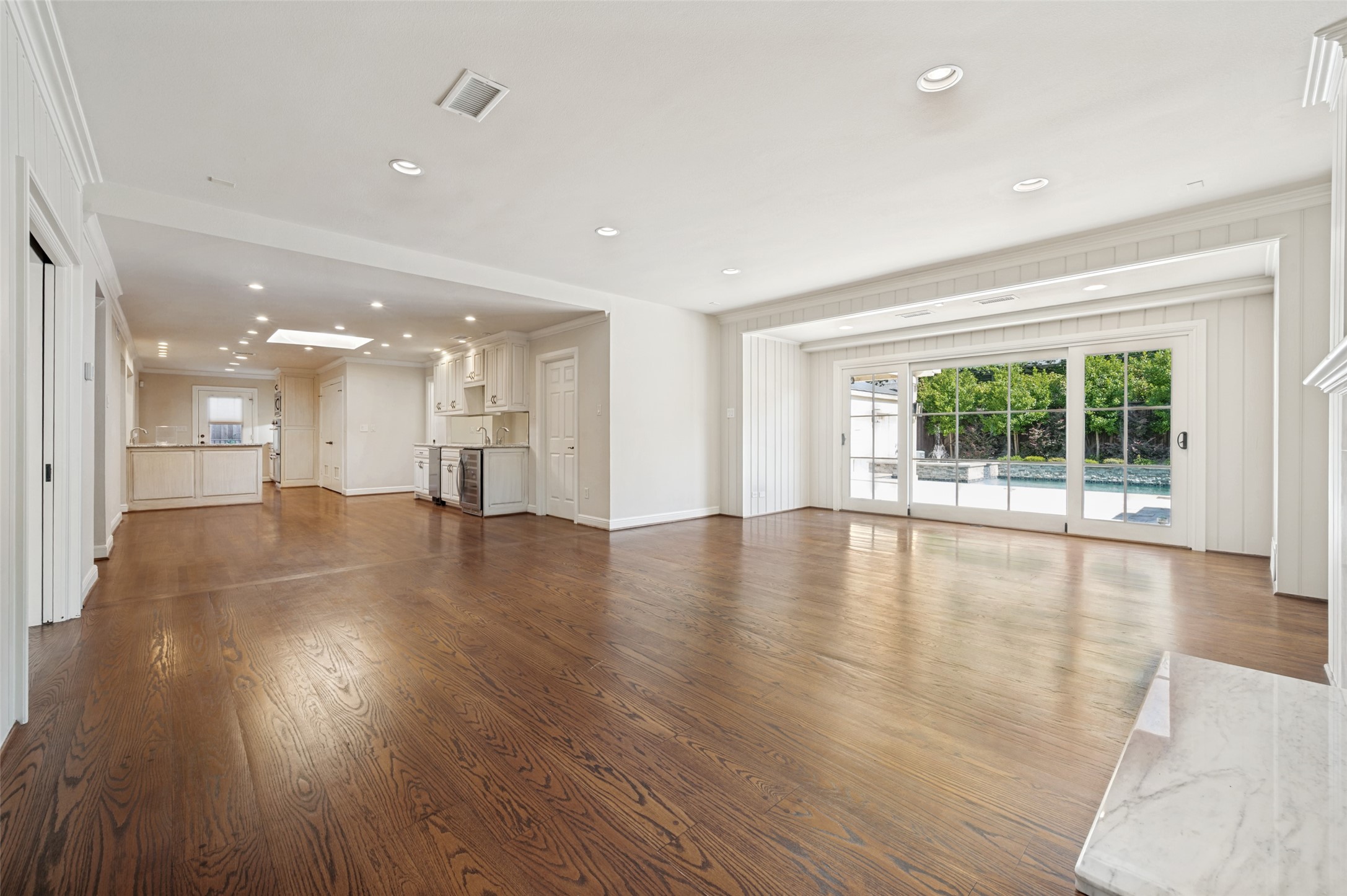Open-plan living area with hardwood floors, kitchen, and glass doors overlooking a pool.