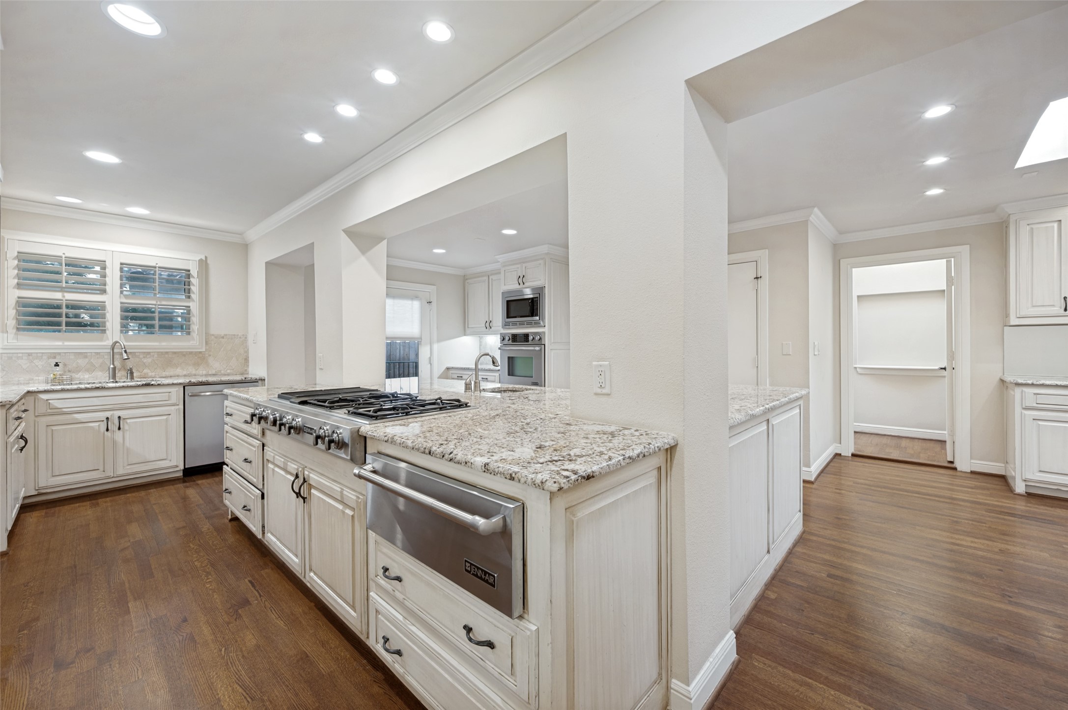Kitchen with white cabinetry, granite island, gas cooktop, and hardwood floors.