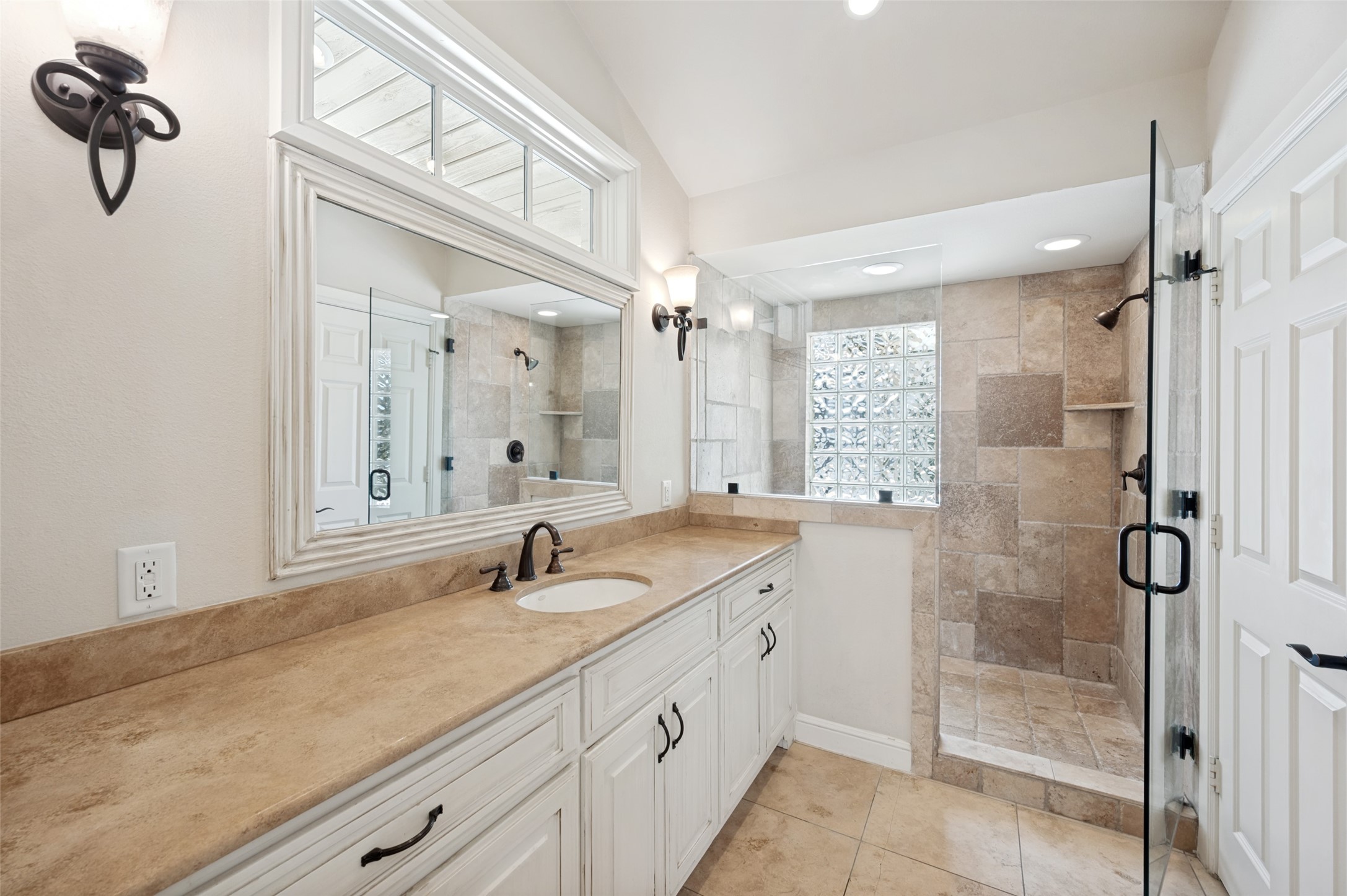 Bathroom with a long stone vanity and a glass-enclosed shower with a glass-block window.