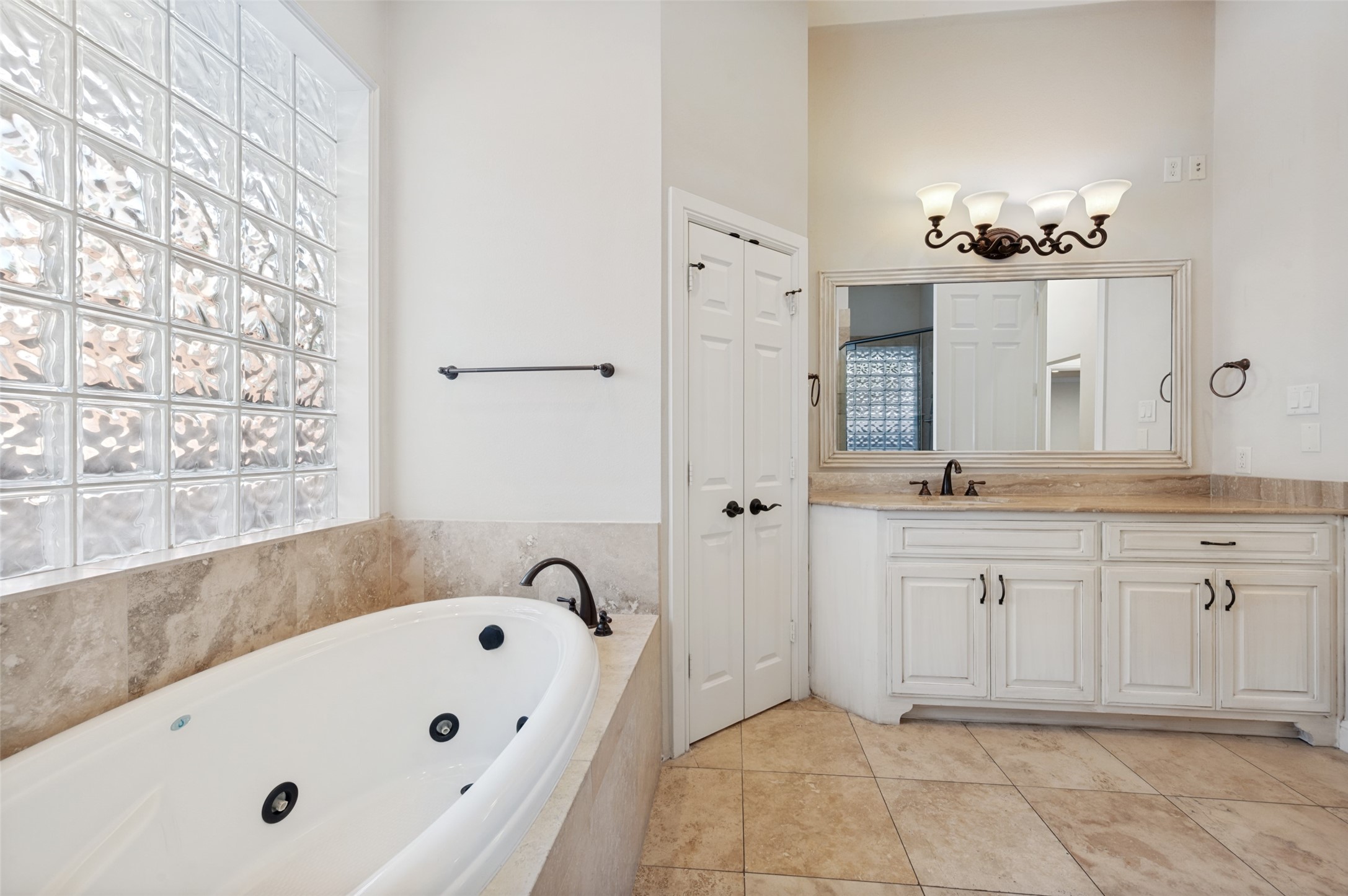 Bathroom with a jetted soaking tub, glass-block window, and white double vanity.