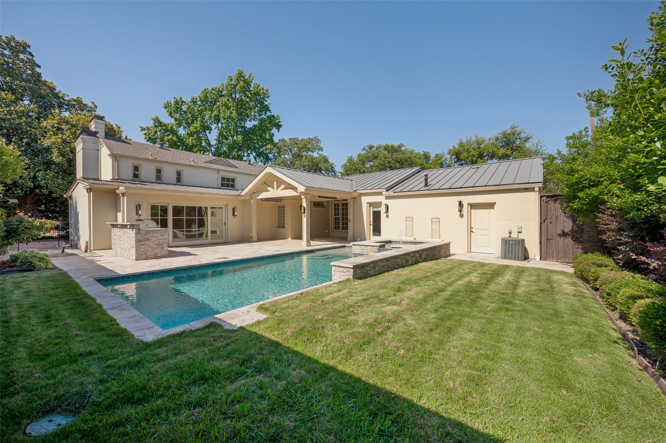 Rear of a cream brick home with a covered patio and stone-edged pool.