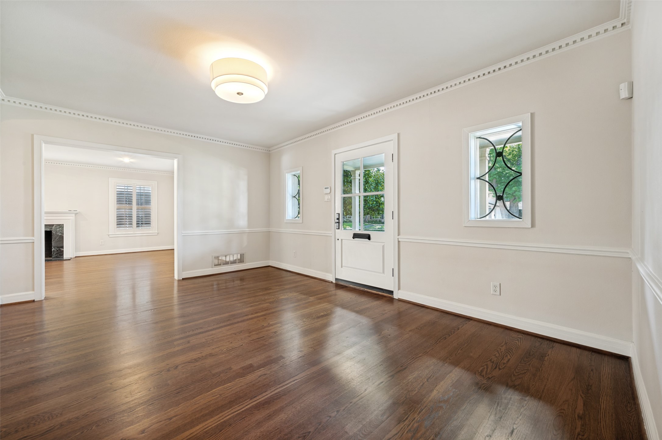 Entry room with dark hardwood floors, decorative windows beside the front door, and an adjoining room with a fireplace.