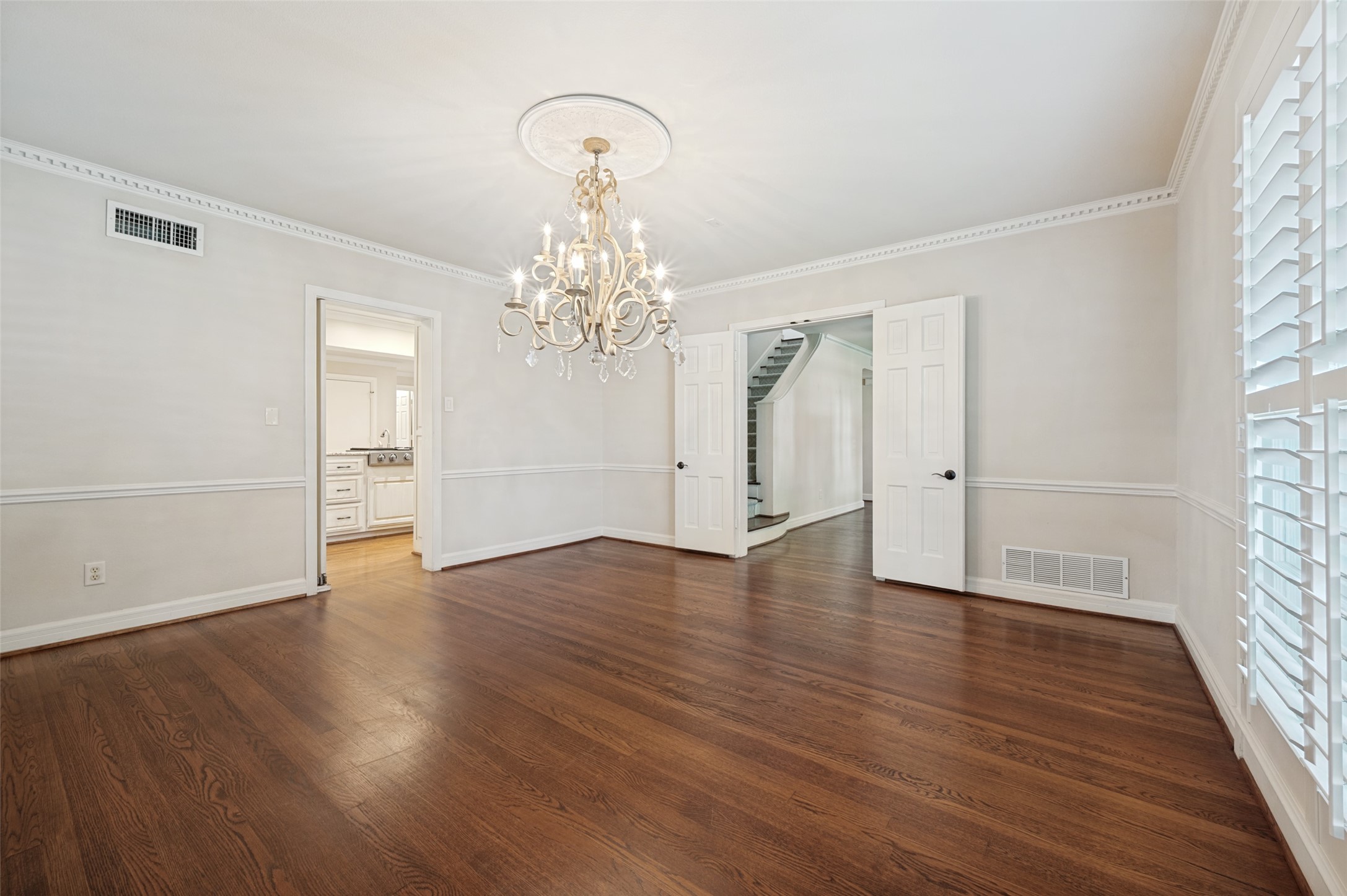 Empty dining room with hardwood floors, crystal chandelier, and plantation shutters.