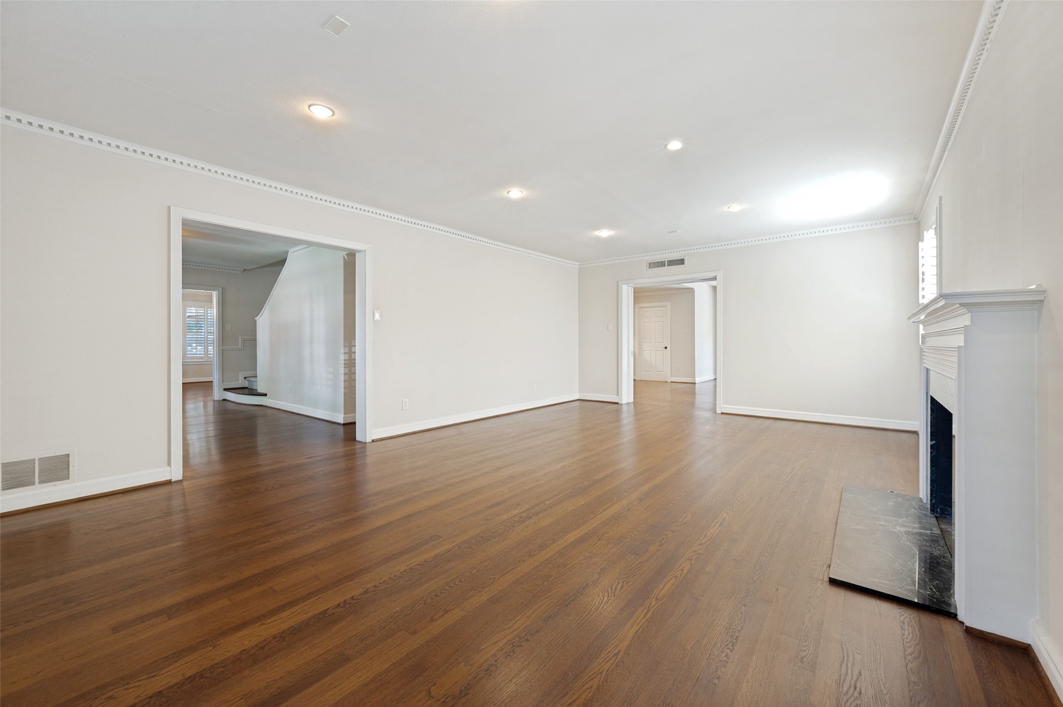 Vacant living room with hardwood floors, a white fireplace, and an opening to the staircase.
