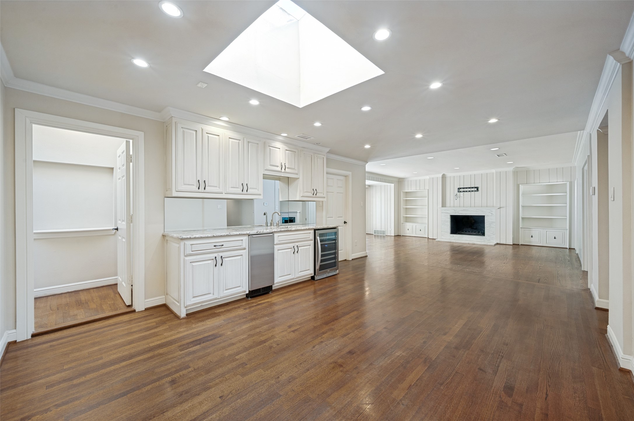 Open kitchen and living area with white cabinets, hardwood floors, skylight, and marble fireplace.