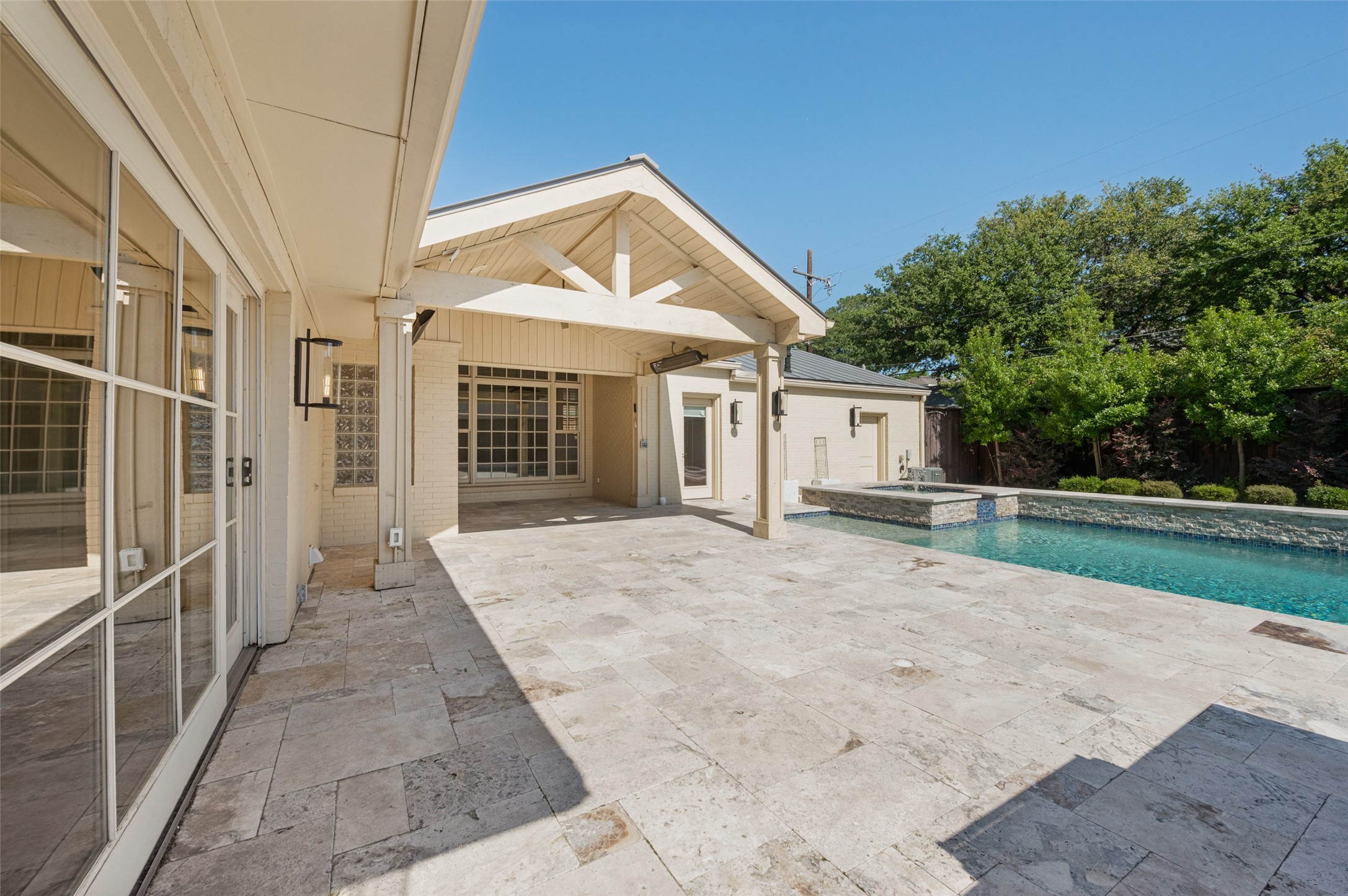 Stone patio and swimming pool beside a cream home with a covered outdoor area.