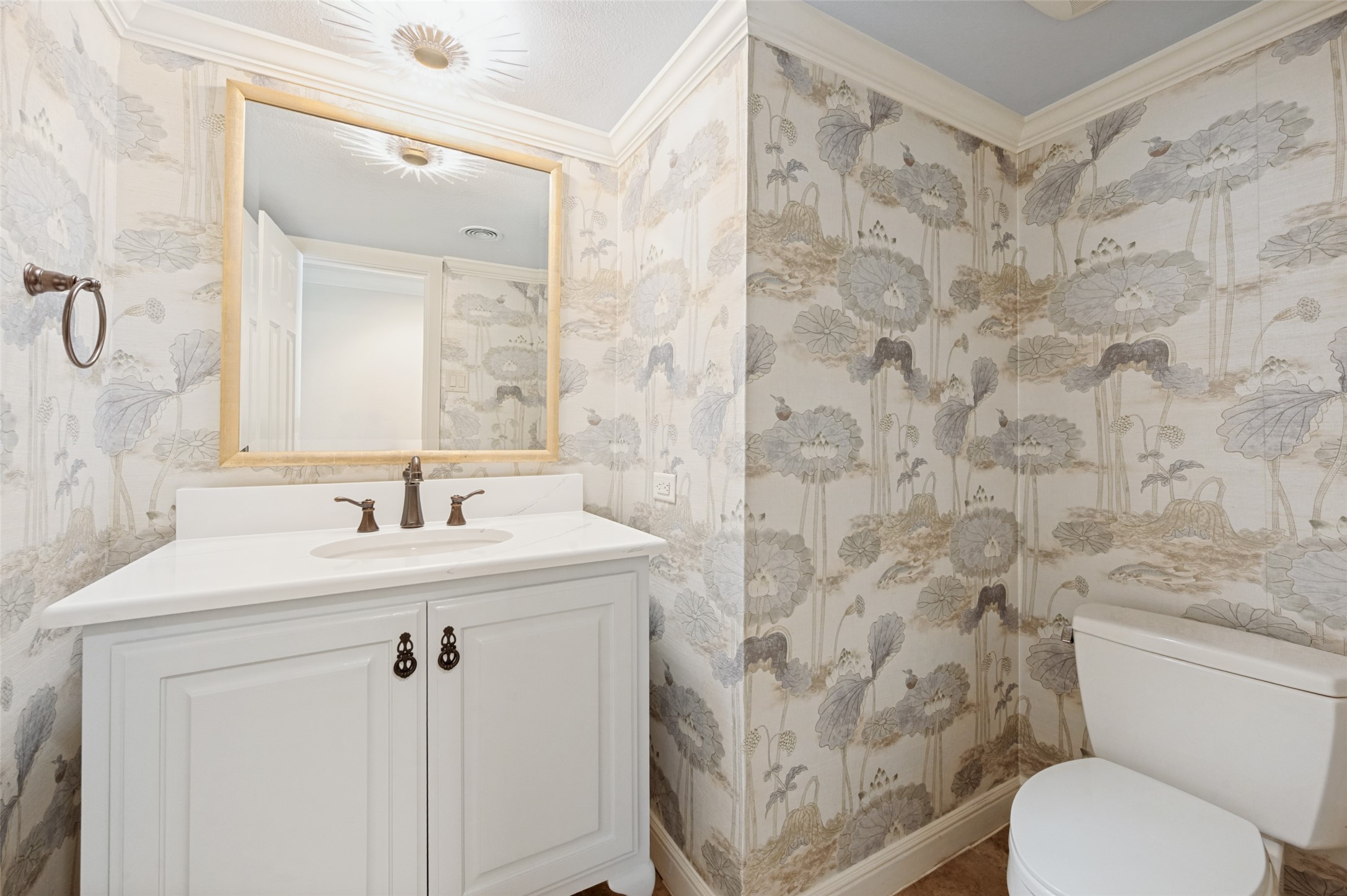 Bathroom with a white vanity, gold-framed mirror, and gray floral wallpaper.