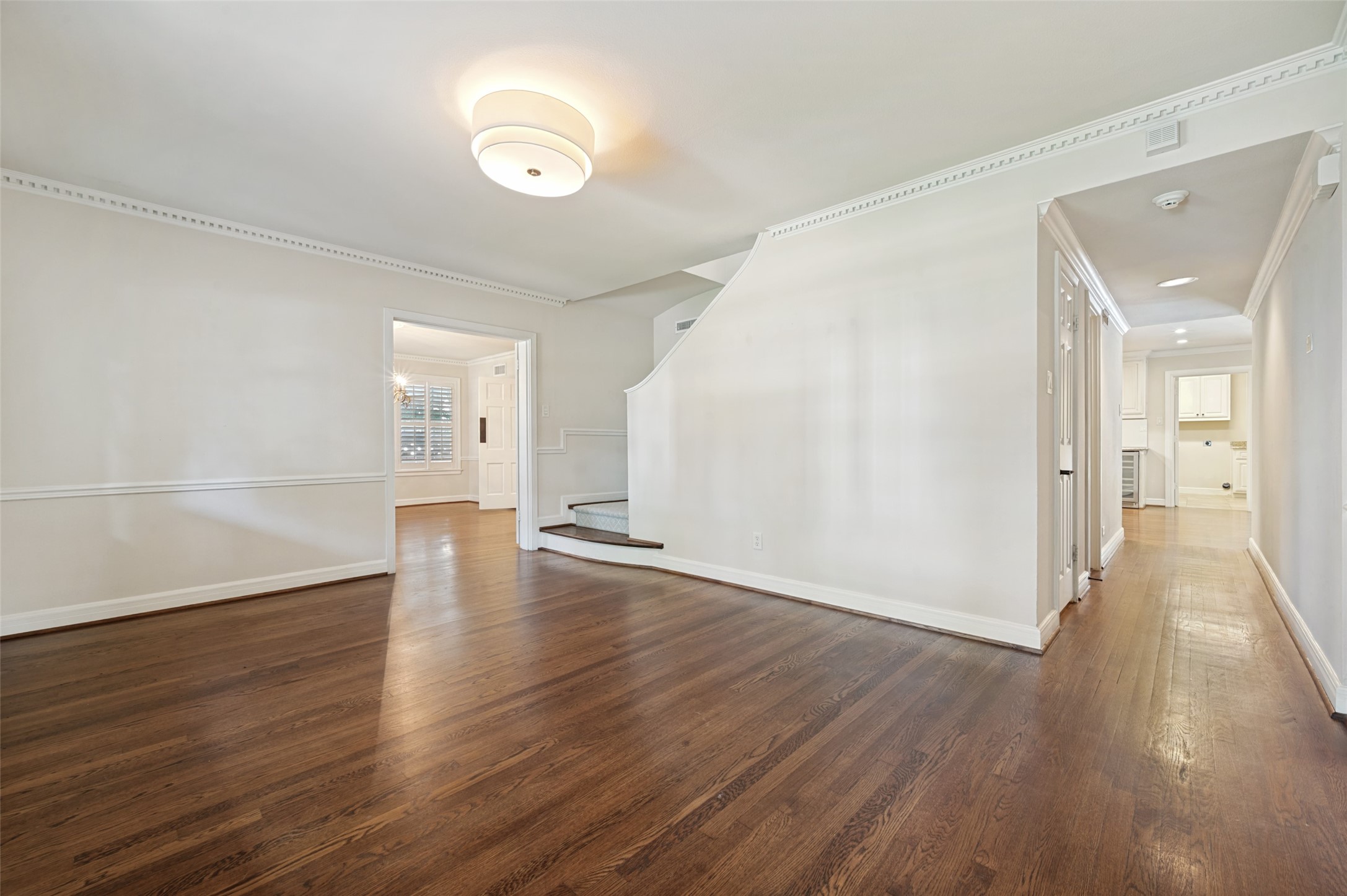 Empty living room with hardwood floors, decorative molding, and a curved staircase beside the hallway.