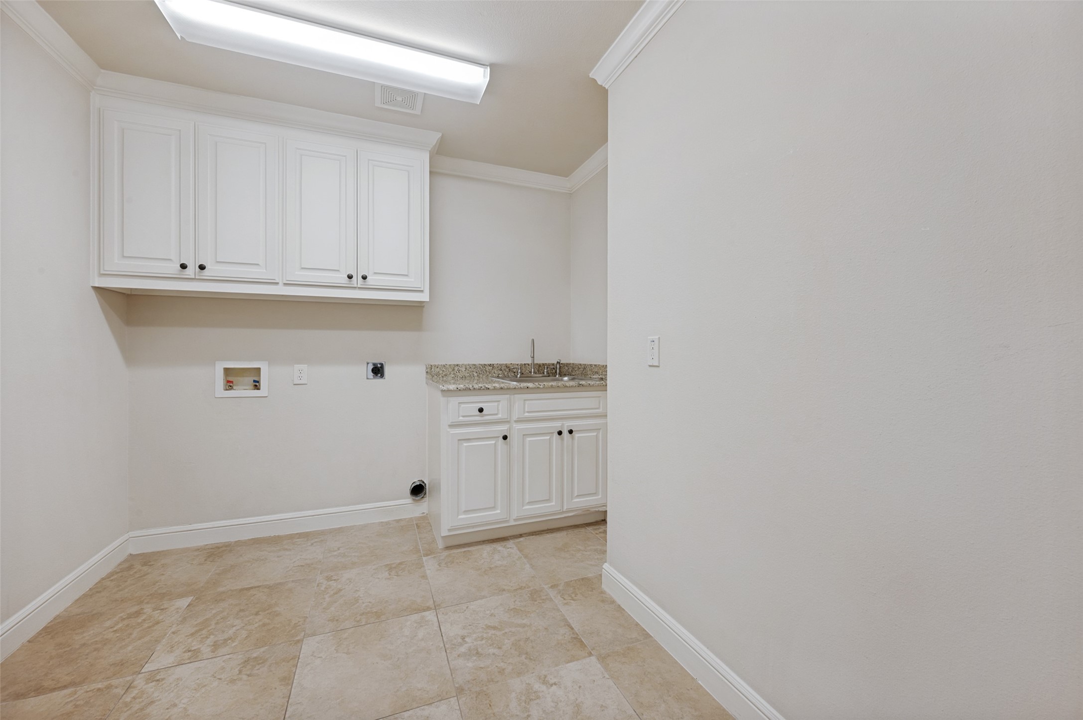 Empty laundry room with white cabinets, granite counter, sink, and tan tile floor.