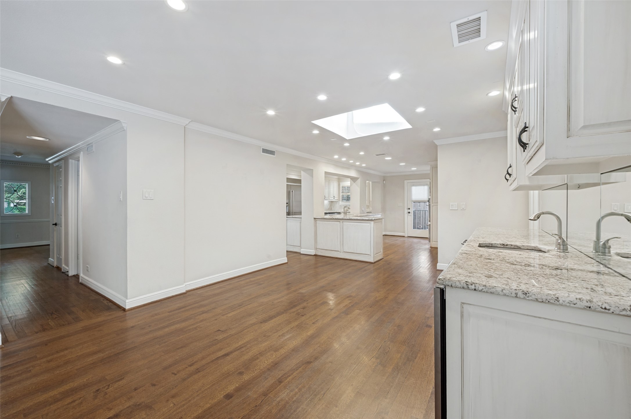 Open kitchen with white cabinets, granite counters, a skylight, and hardwood floors.