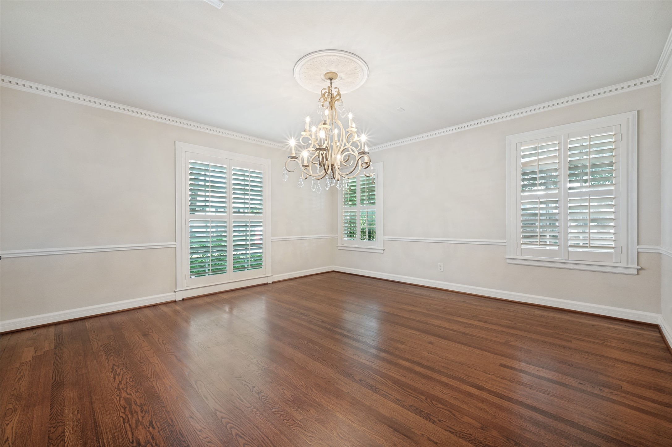 Empty dining room with hardwood floors, shuttered windows, and a chandelier.