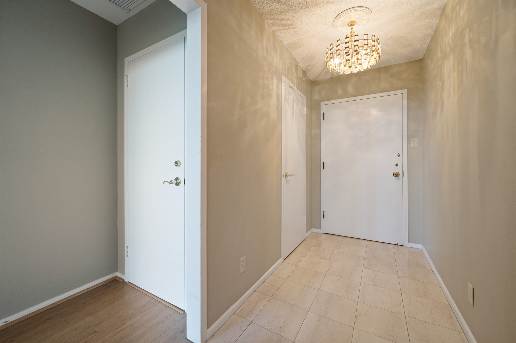 Condominium entry hall with a crystal chandelier, tiled floor, and white front door.