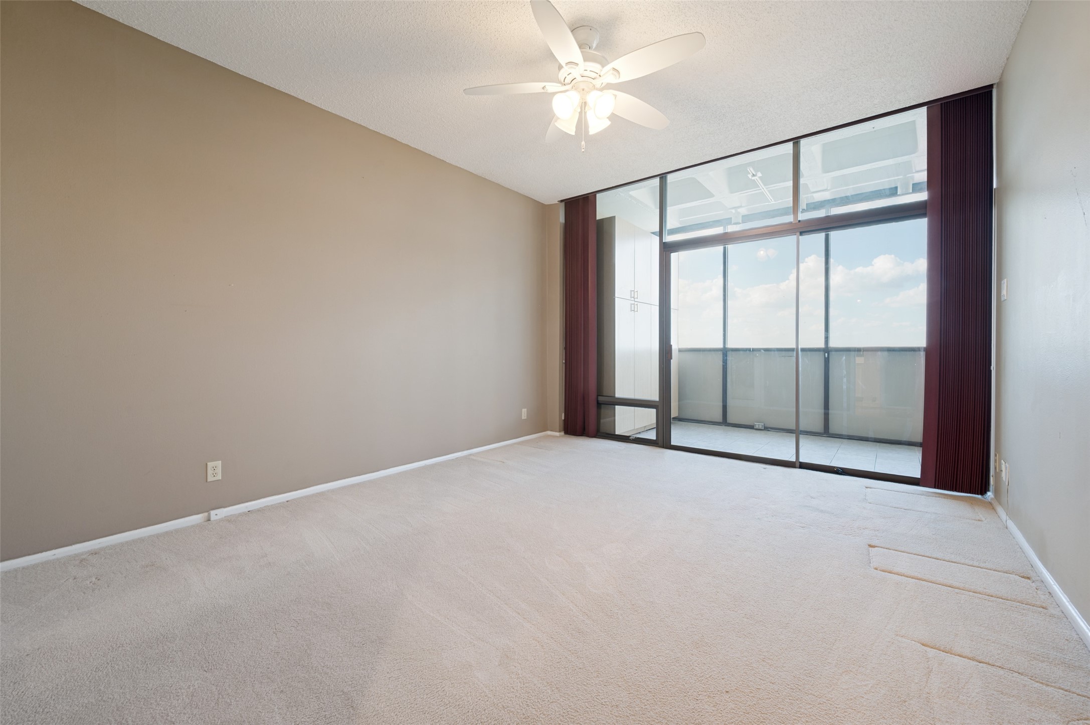 Empty carpeted room with a ceiling fan and sliding glass doors to a balcony.