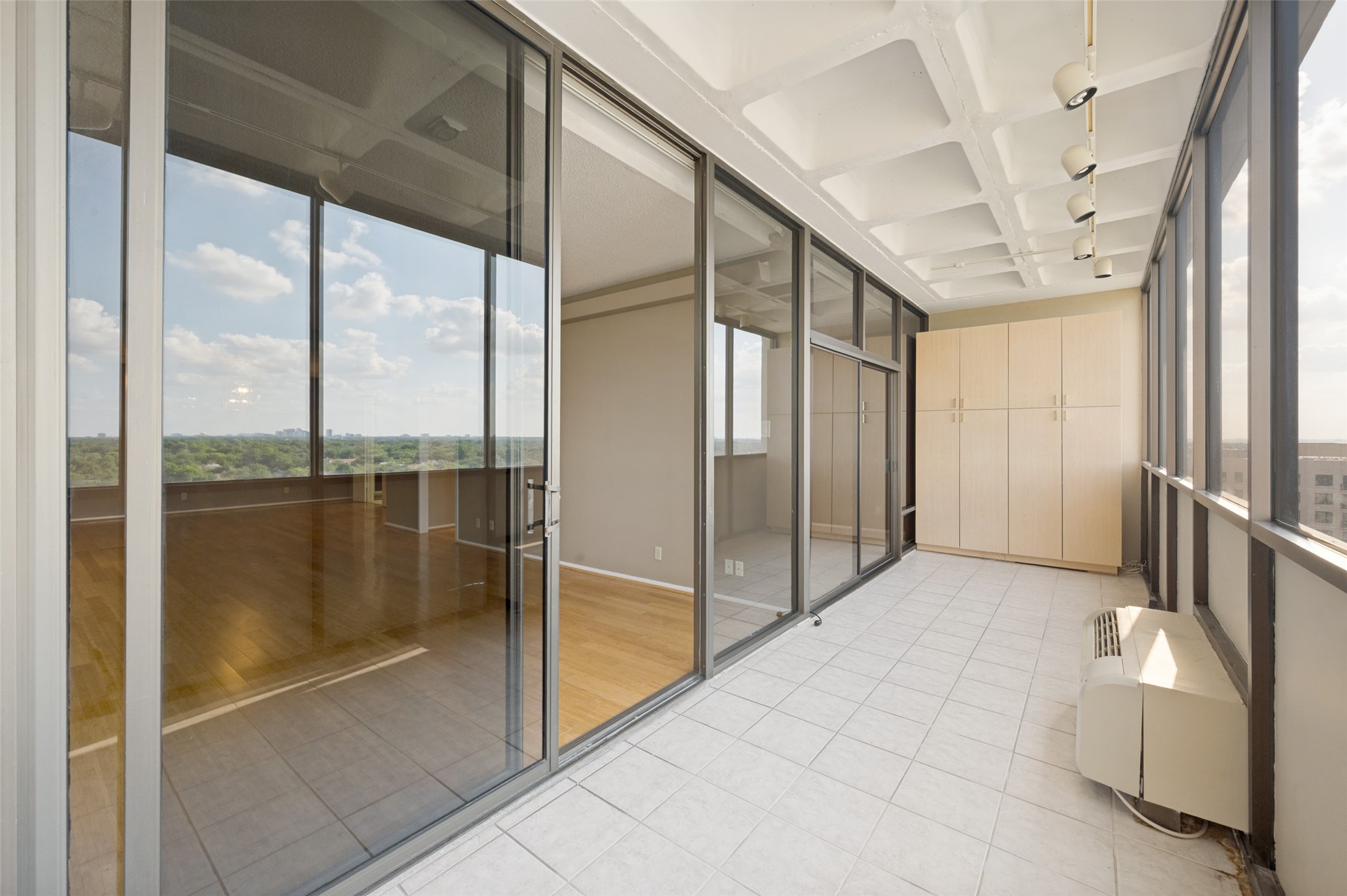 Enclosed balcony with tiled floors, built-in cabinets, and expansive windows overlooking treetops.