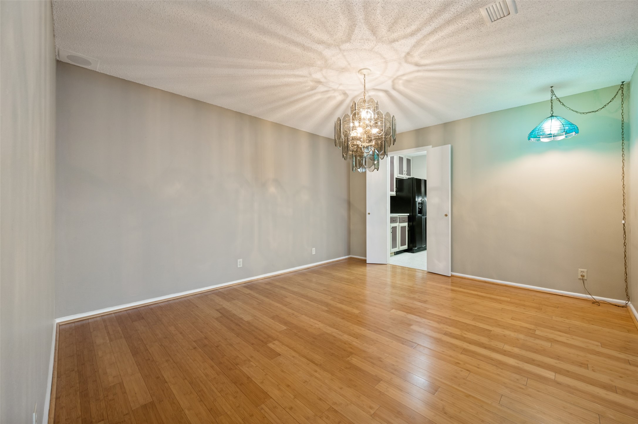 Empty dining area with hardwood floors, a crystal chandelier, and a blue pendant light.