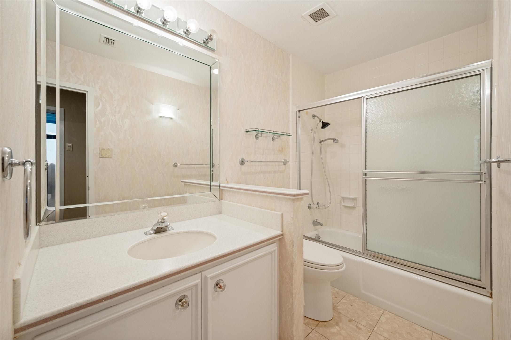 Bathroom with a white vanity, large mirror, and tub-shower with frosted sliding doors.