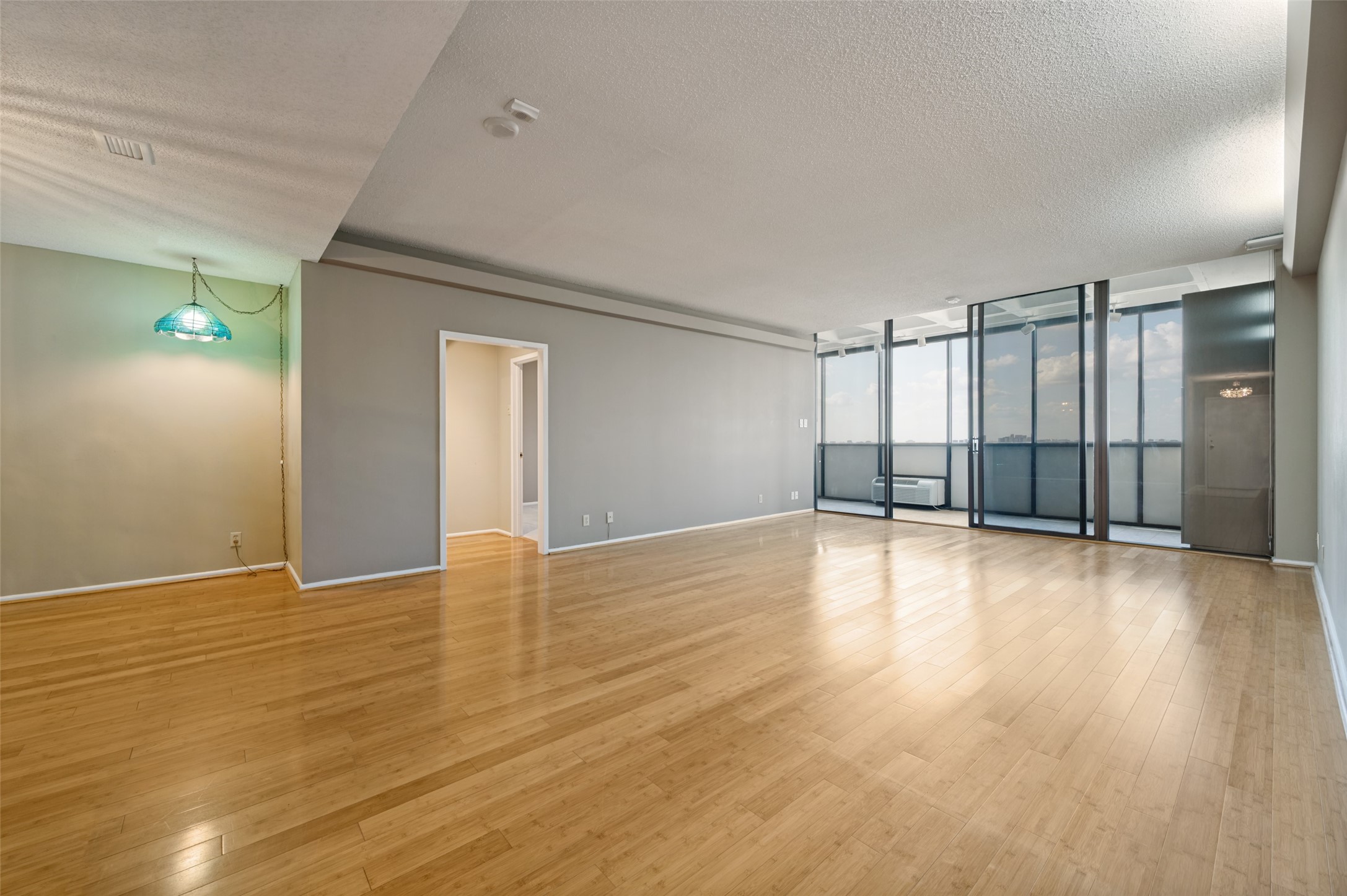 Empty condo living room with wood floors, floor-to-ceiling windows, and a city skyline view.