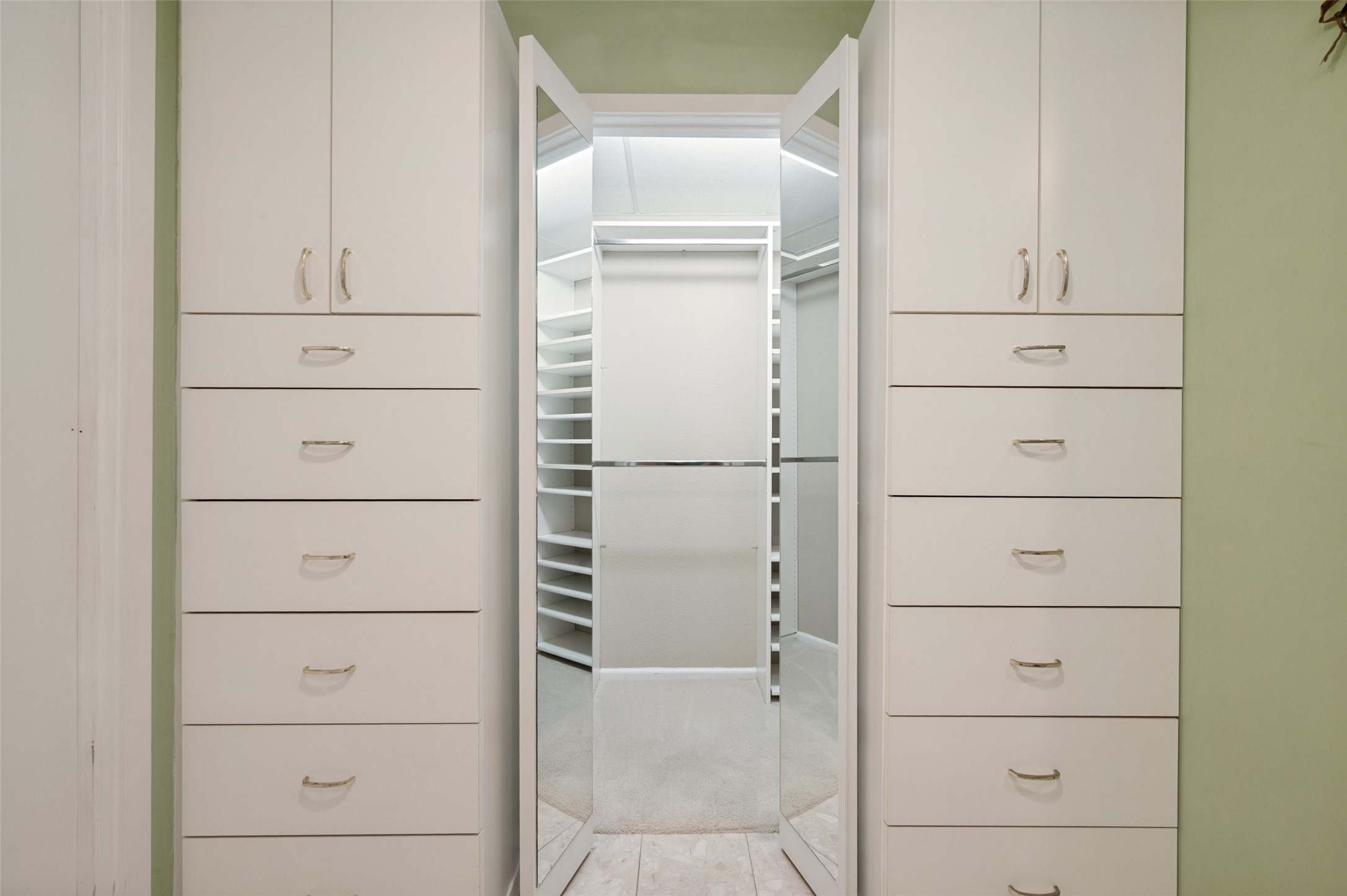 Walk-in closet with white built-in drawers, open shelving, and mirrored doors.