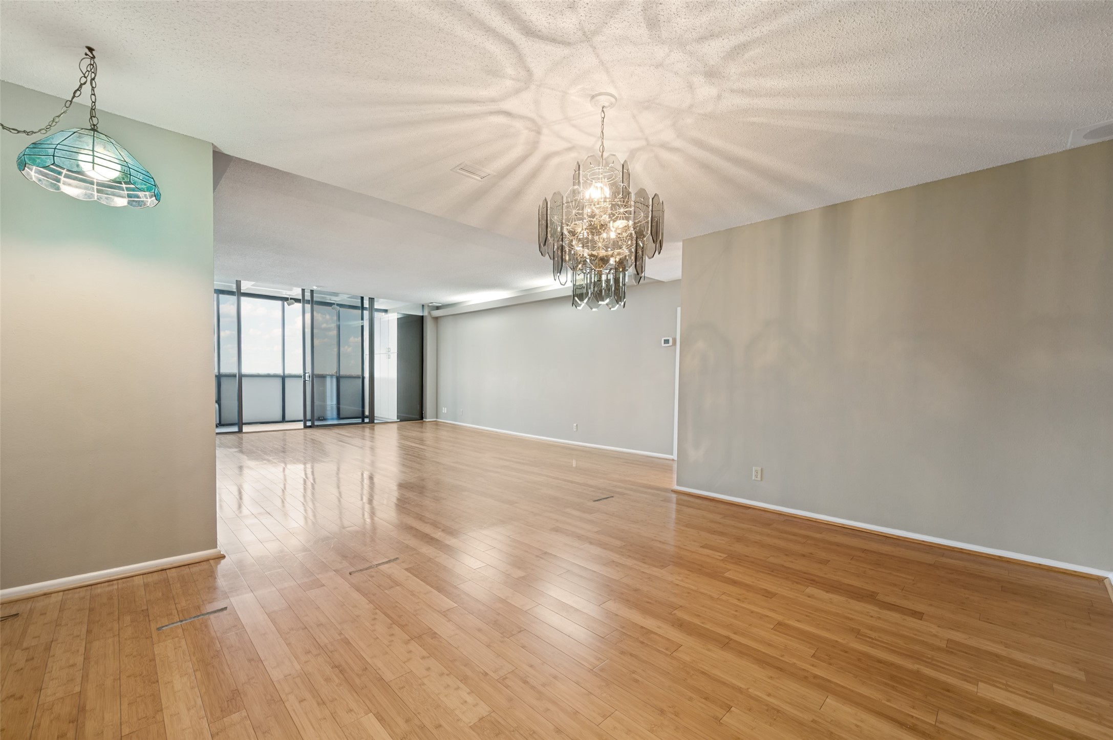 Vacant living and dining area with wood floors, two chandeliers, and glass balcony doors.