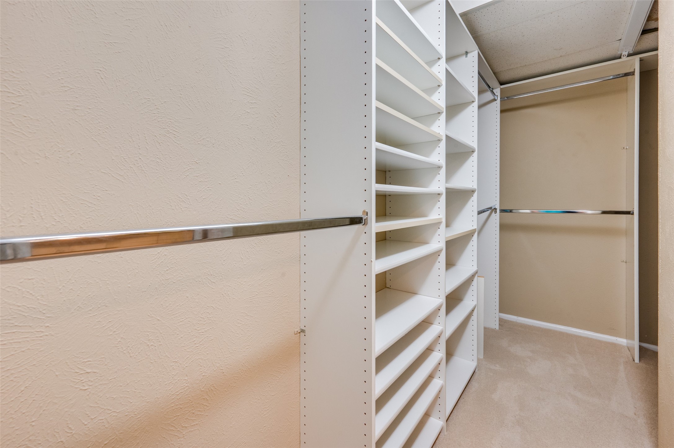 Walk-in closet with built-in white shelves and chrome hanging rods.