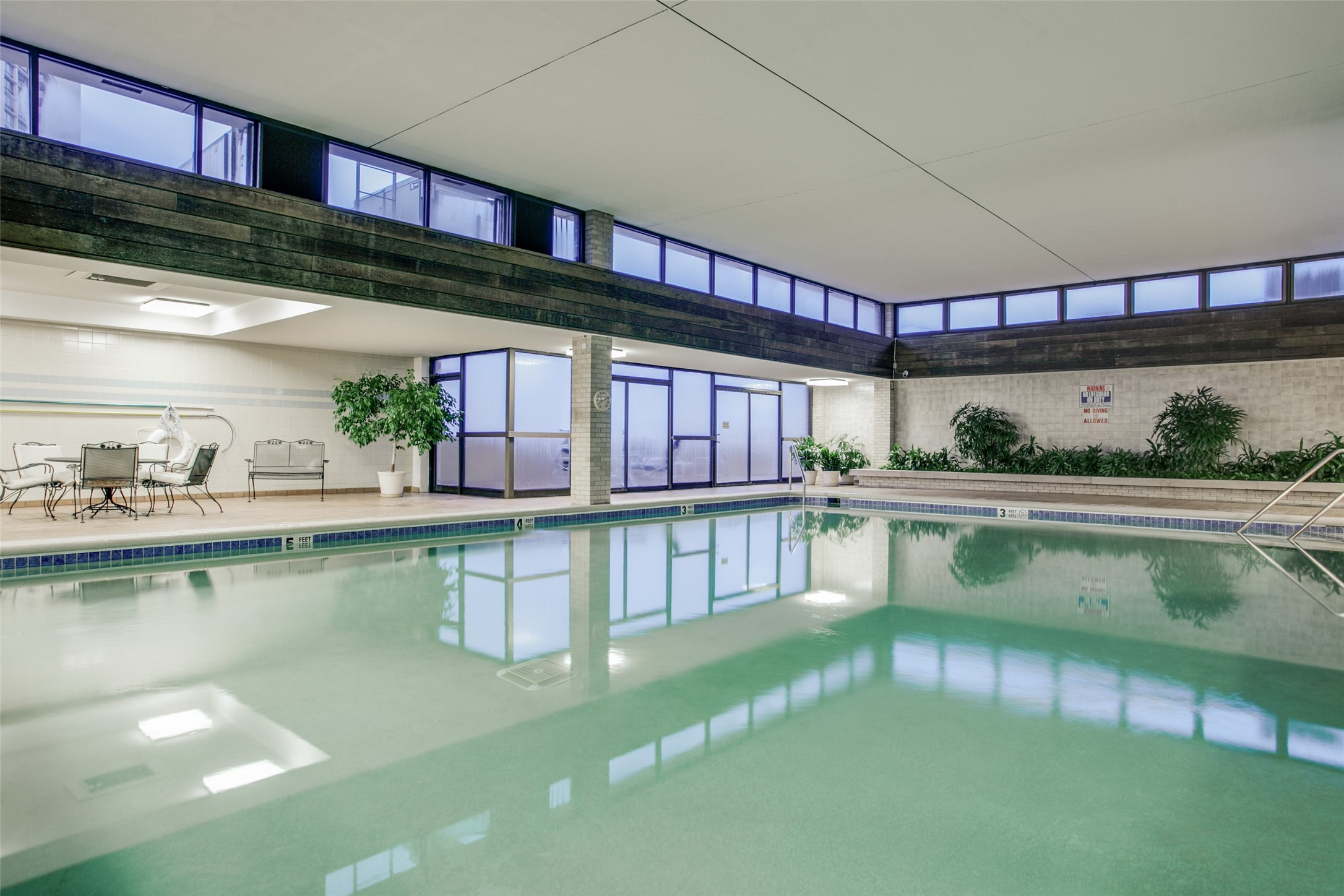 Indoor swimming pool with large windows, tiled deck, and patio seating.