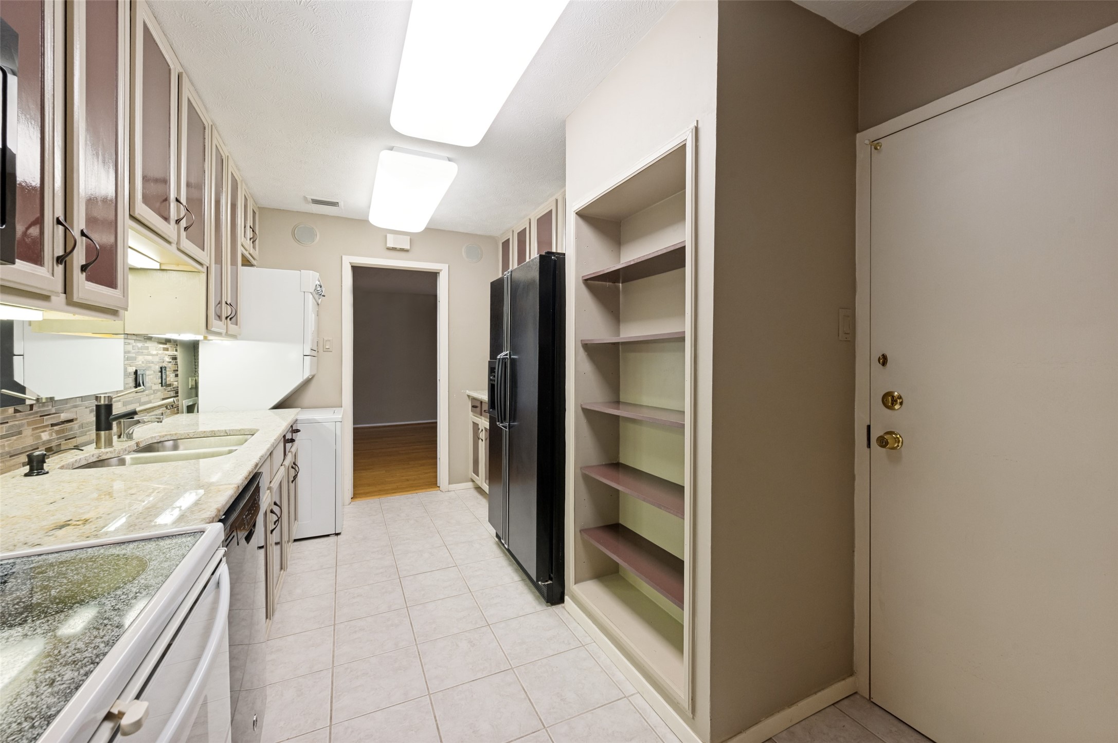 Galley kitchen with granite counters, tiled backsplash, black refrigerator, and tall open shelving.