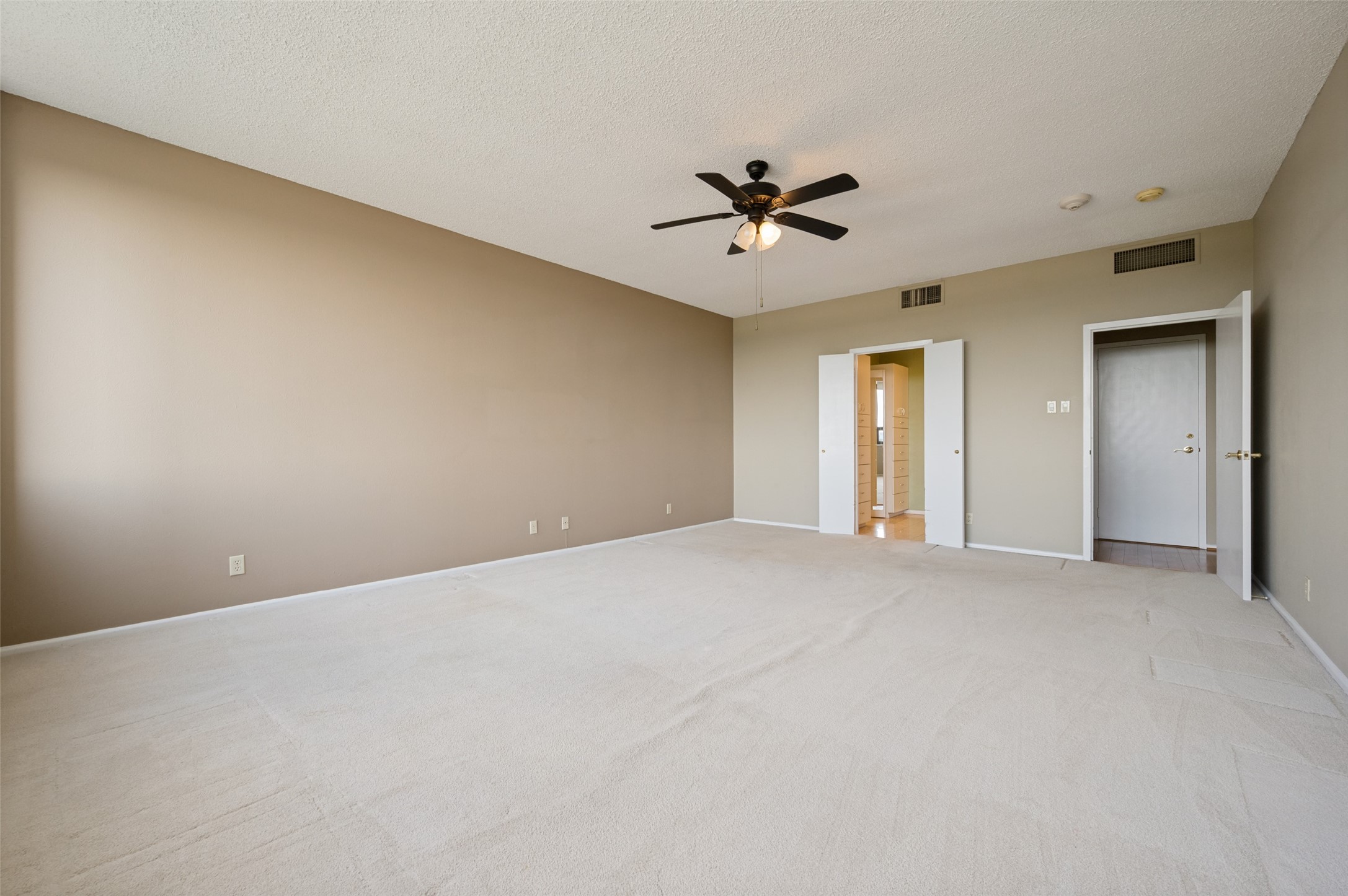 Empty carpeted bedroom with a ceiling fan and open doors to a walk-in closet.