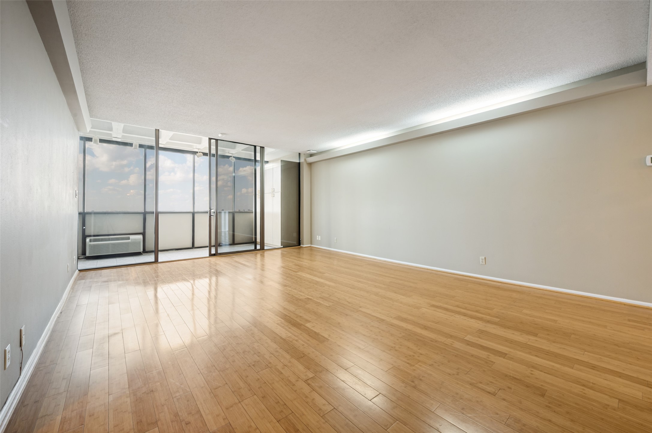 Empty living room with wood floors and floor-to-ceiling glass doors opening to a balcony.
