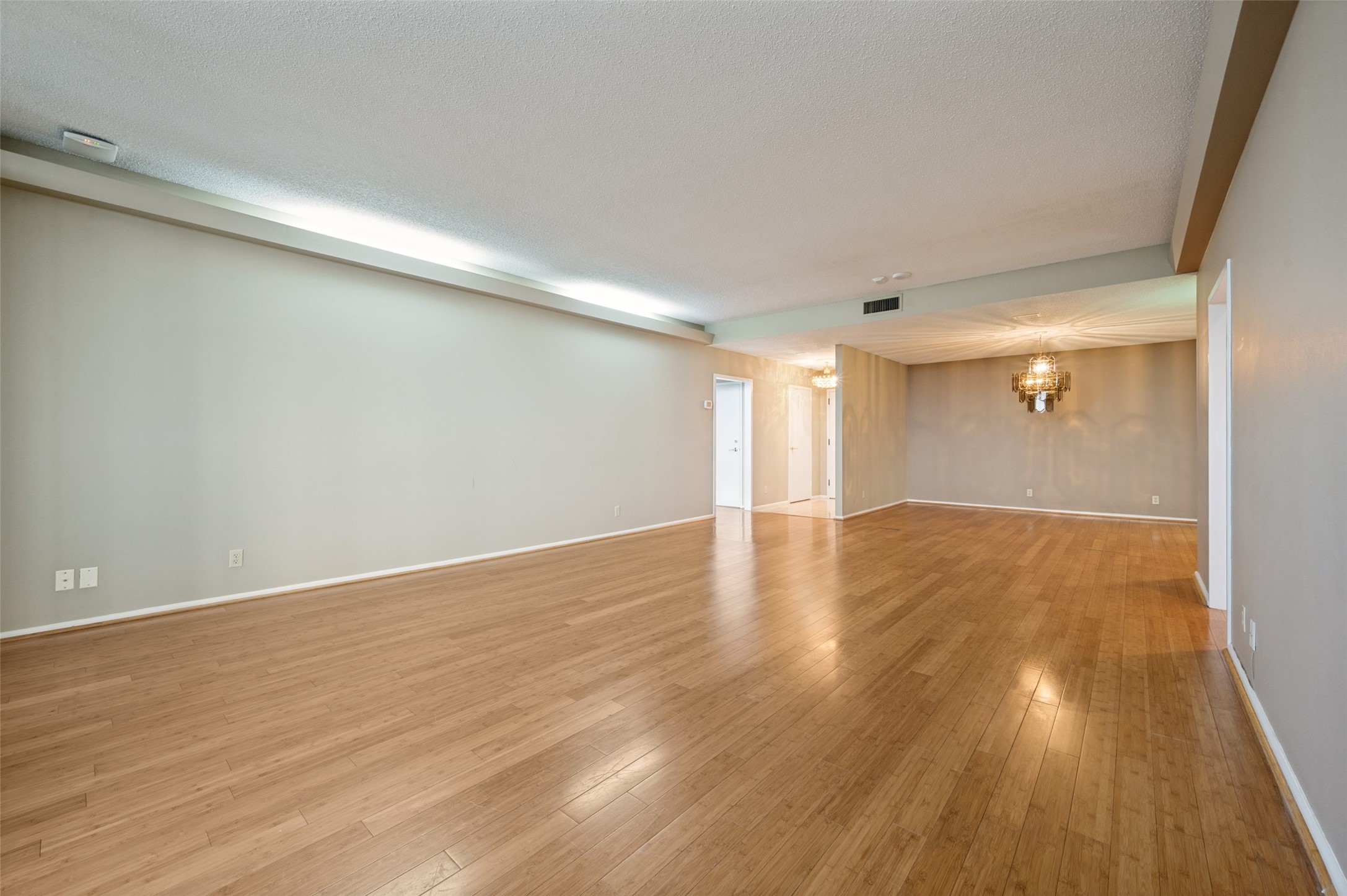 Vacant living and dining area with warm wood floors and a chandelier.