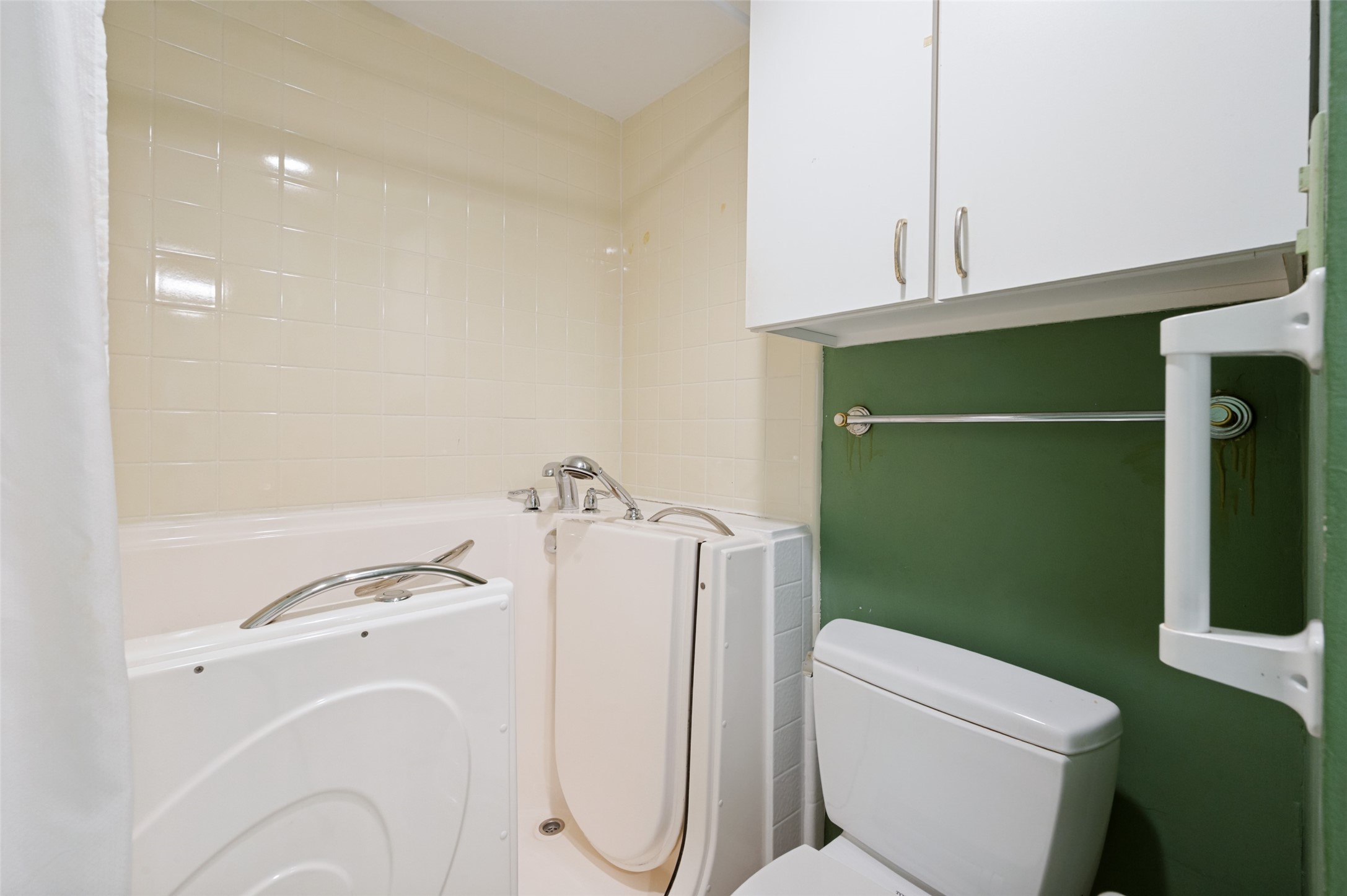 Bathroom with a walk-in tub, toilet, cream tile, and dark green accent wall.