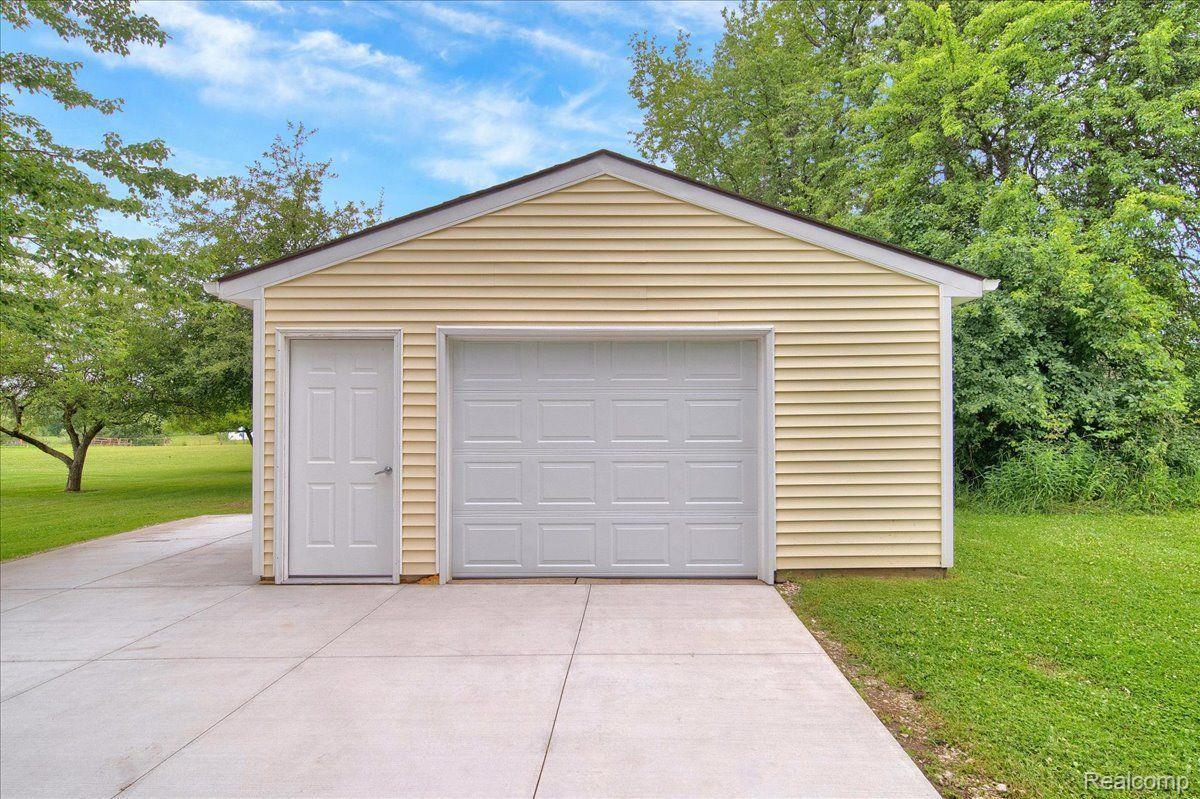 Detached beige garage with a white double door, separate entry door, and wide concrete driveway.