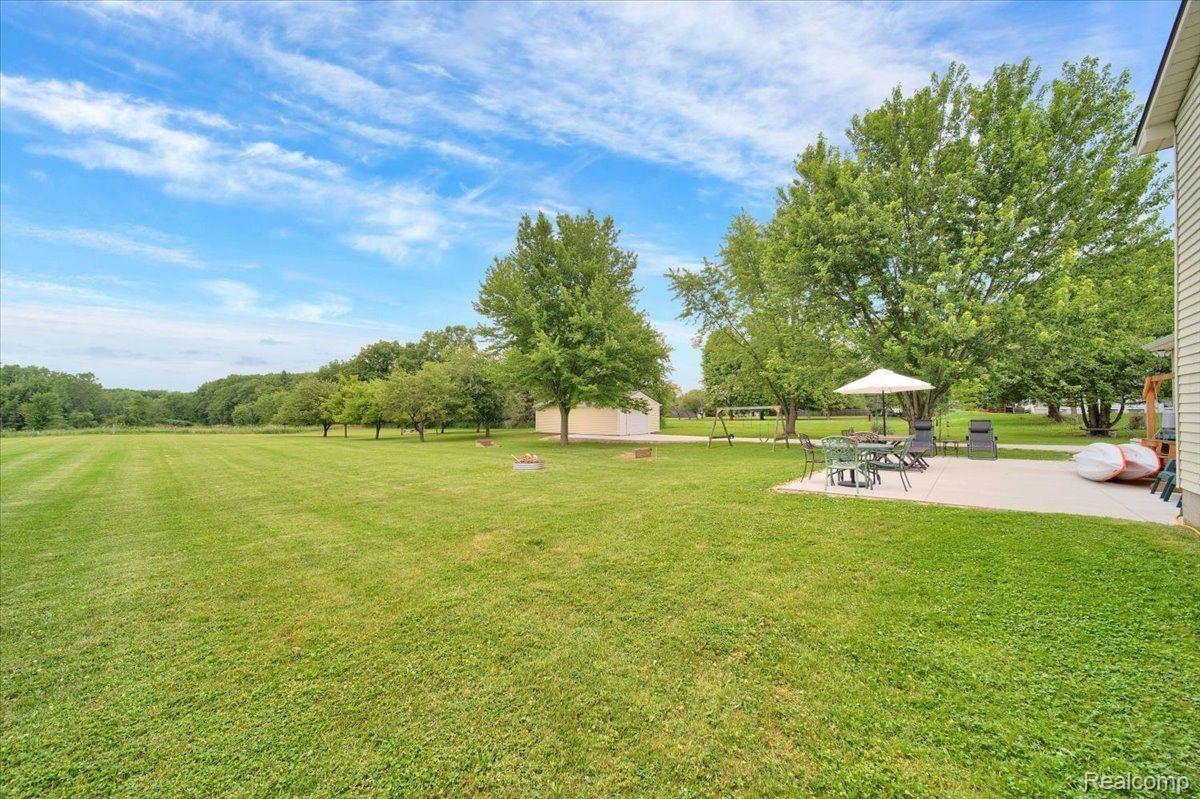 Spacious backyard lawn with mature trees, a small shed, and a patio dining area.