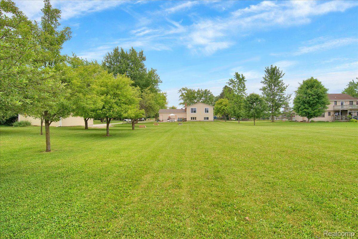 Expansive mowed lawn with mature trees and several houses in the distance.